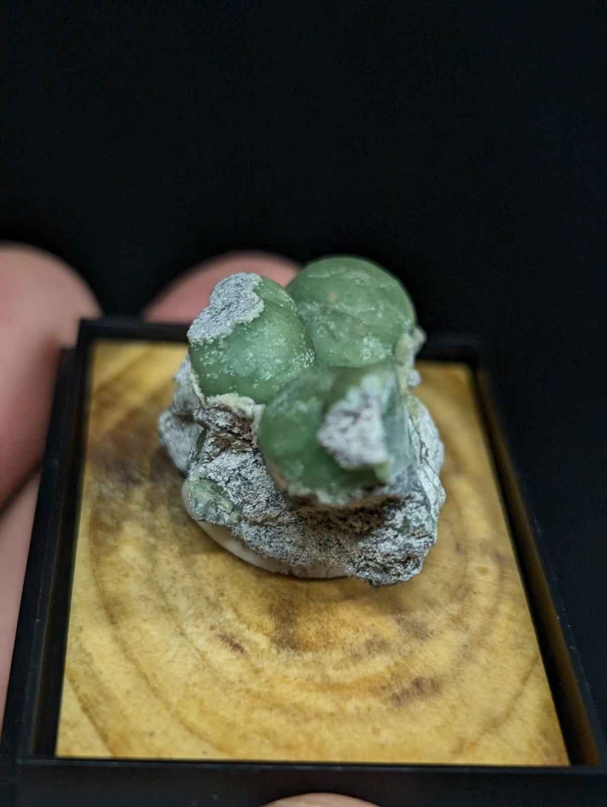 A green, translucent mineral specimen with a rough, grayish matrix and rounded crystalline formations.