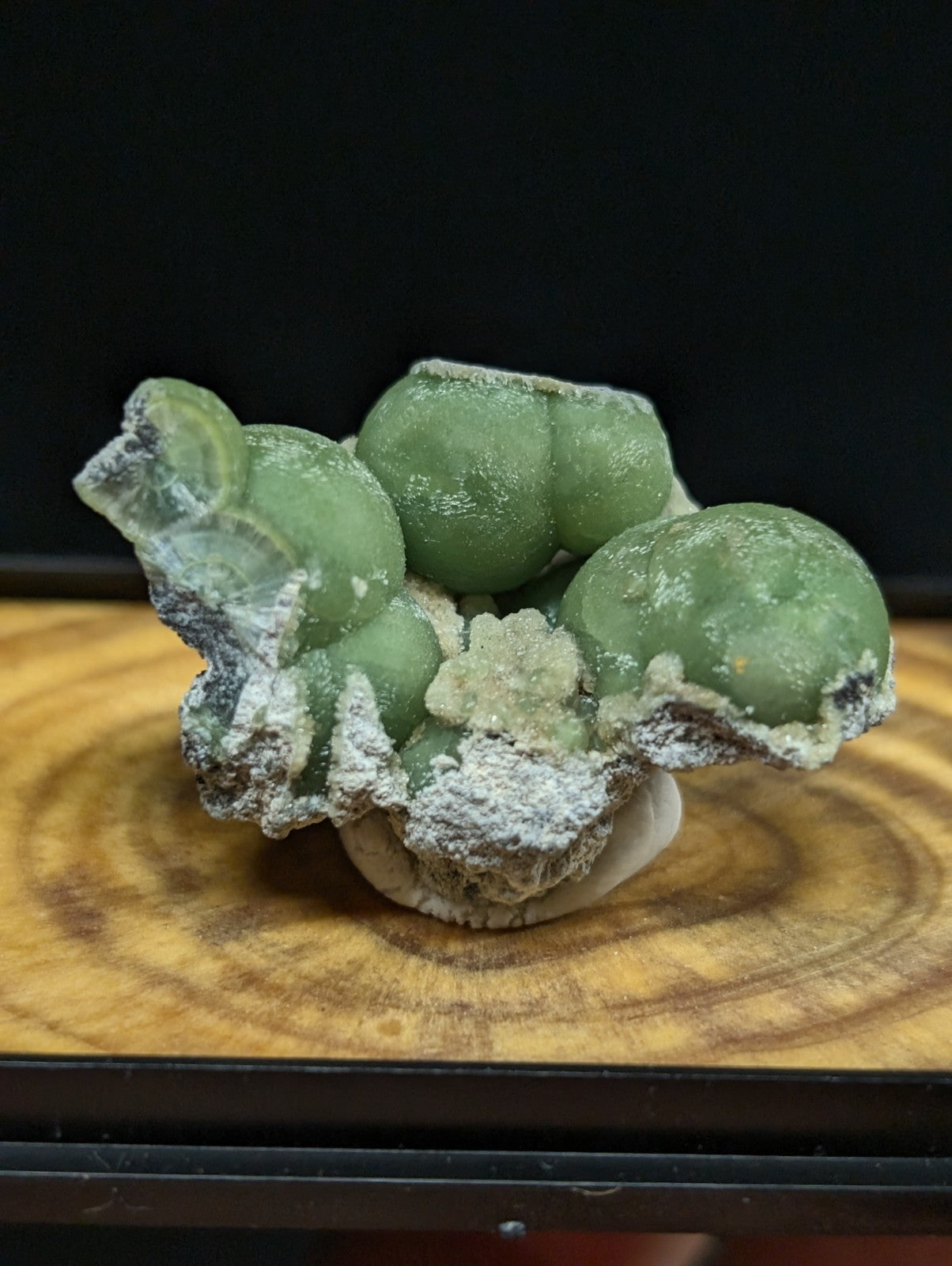 A green, spherical mineral specimen with a crystalline texture and white powdery coating.