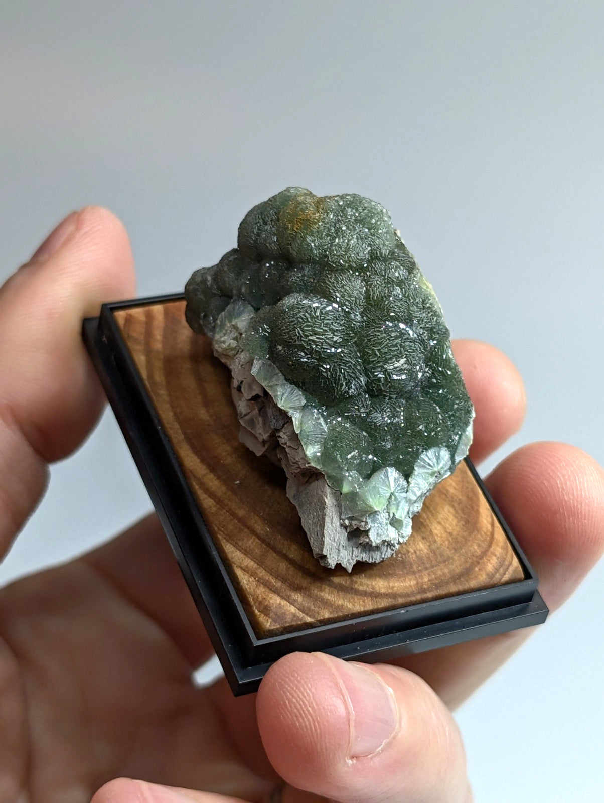 A green, bumpy mineral specimen with translucent crystalline formations rests on a wooden display base.