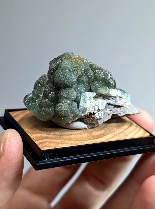 A green, bubbly mineral specimen with a translucent quality and subtle yellowish patches rests on a wooden display base.