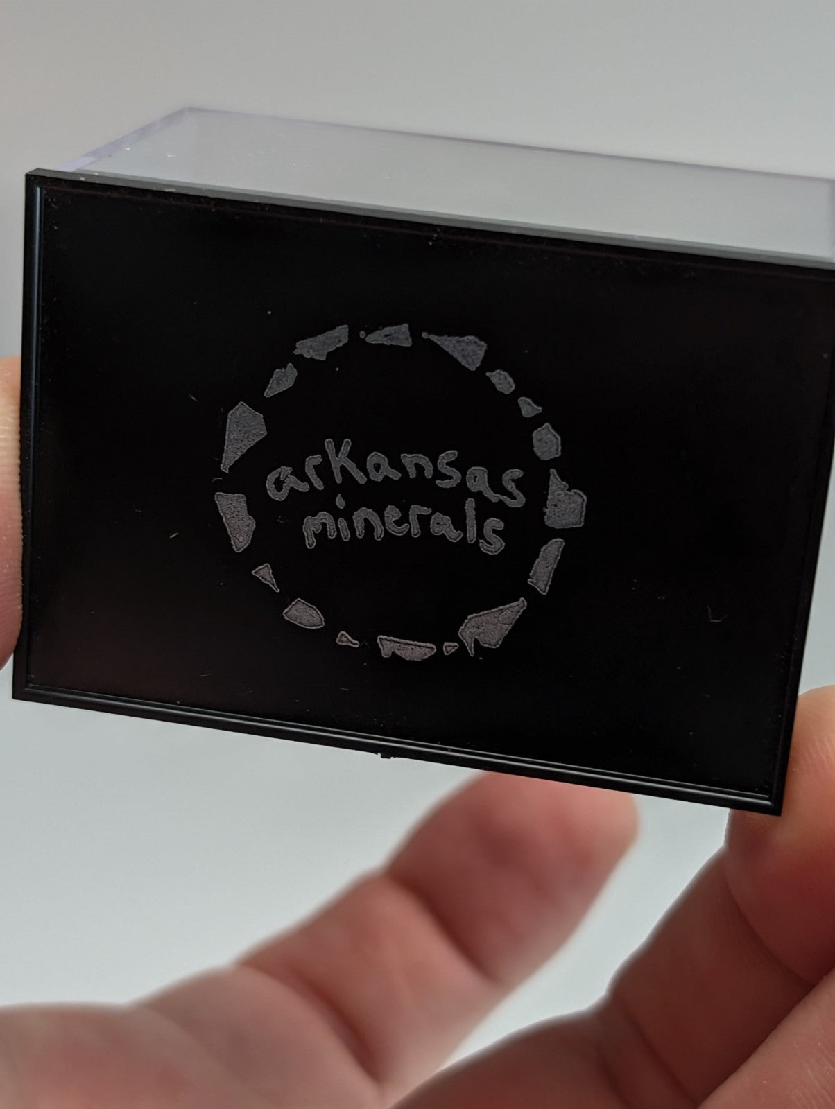 Black rectangular box with ’arkansas minerals’ logo etched in silver, surrounded by a circular pattern of stone shapes.