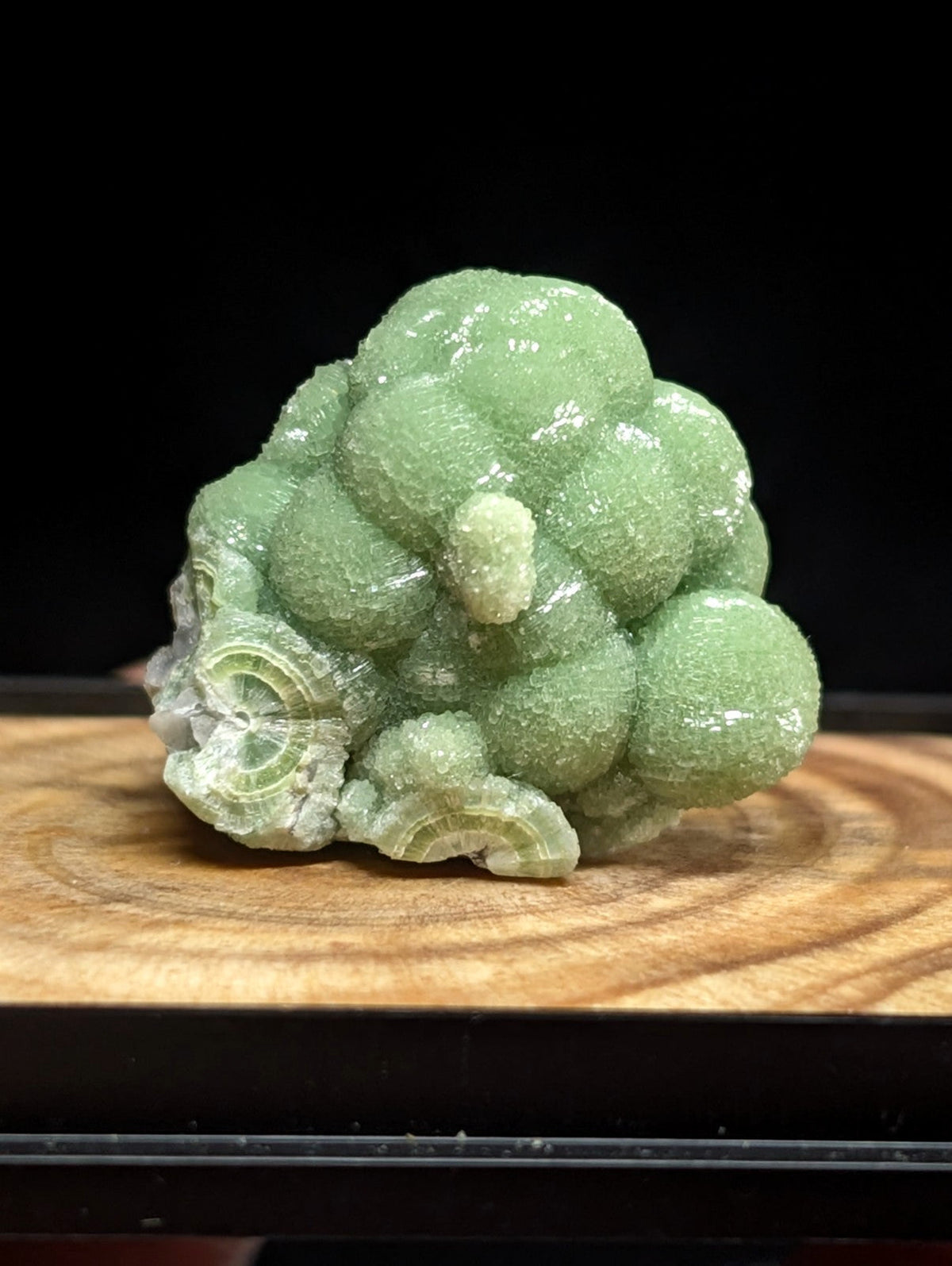 A vibrant green, translucent mineral specimen with a clustered, spherical formation and crystalline texture.