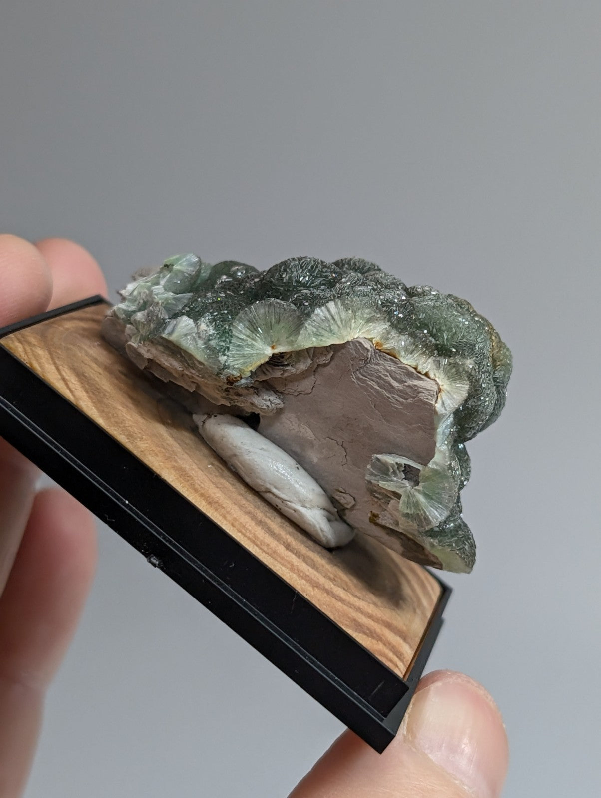 A green, translucent crystal formation with a rough, layered texture and embedded white stone.
