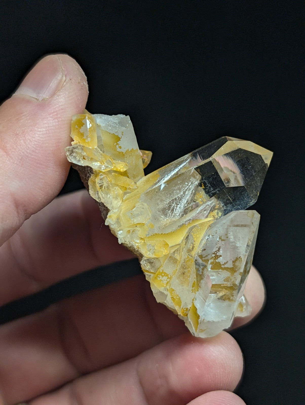 A translucent yellow and clear quartz crystal cluster with sharp, faceted edges held in a hand.