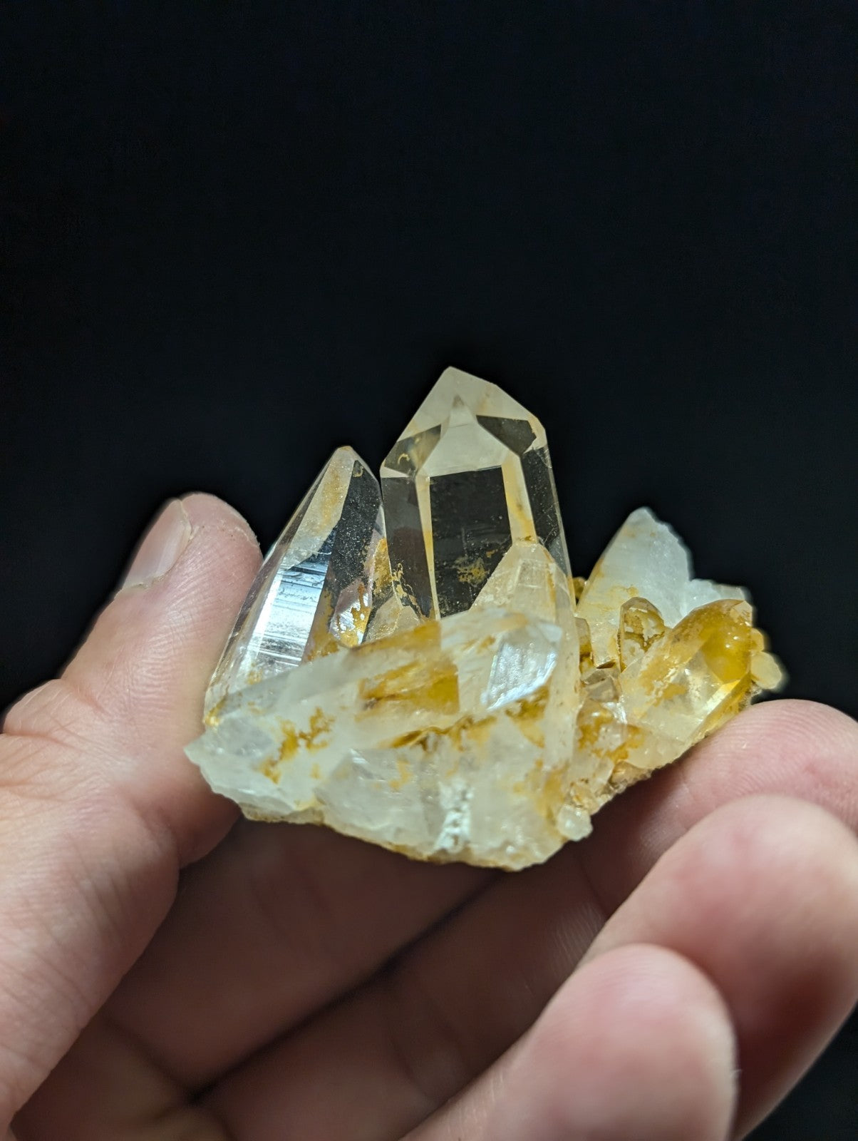 A cluster of translucent yellow and clear quartz crystals with sharp, faceted points held in a hand.