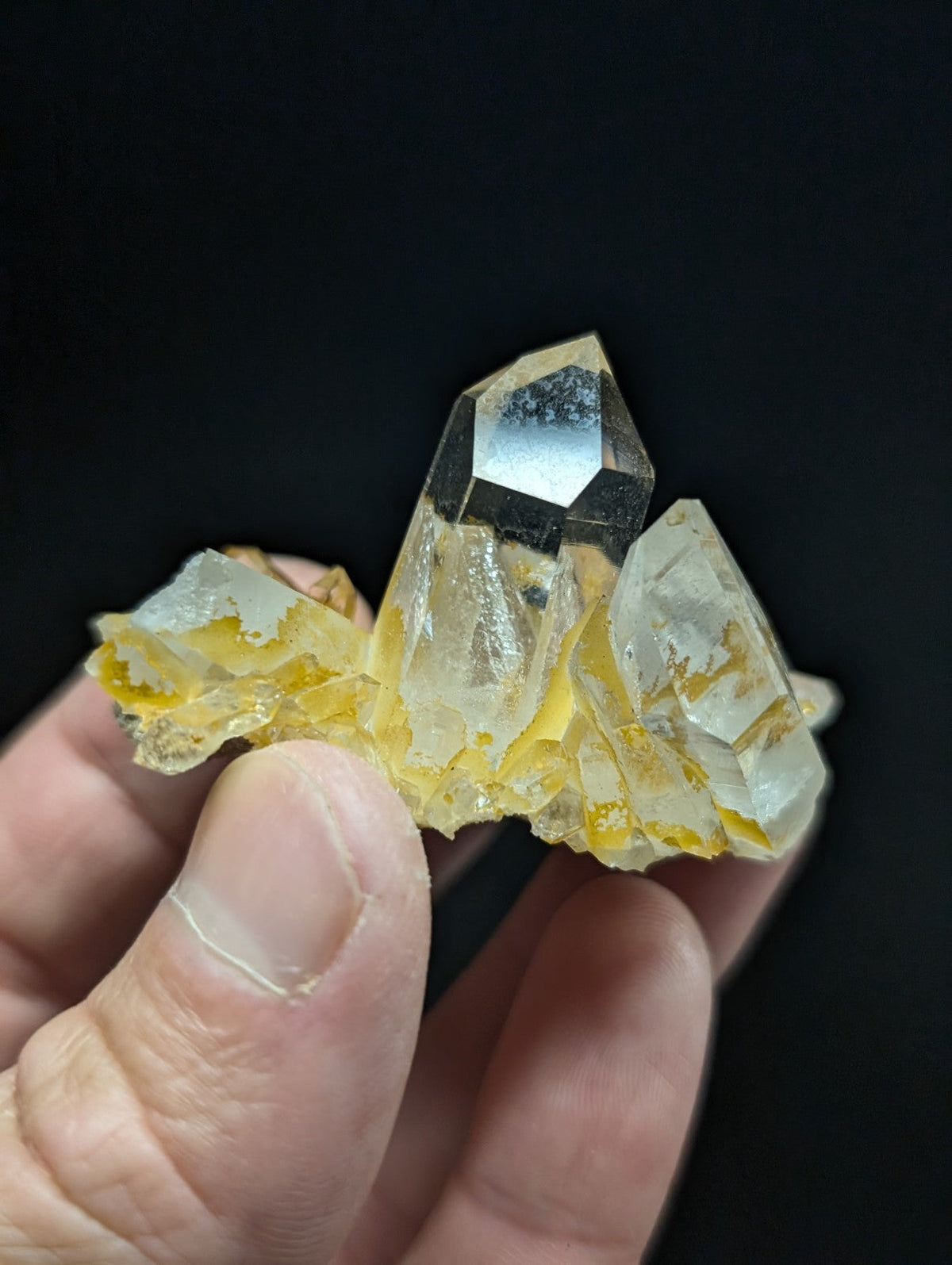 A translucent yellow and clear quartz crystal cluster with sharp, faceted points held in a hand.