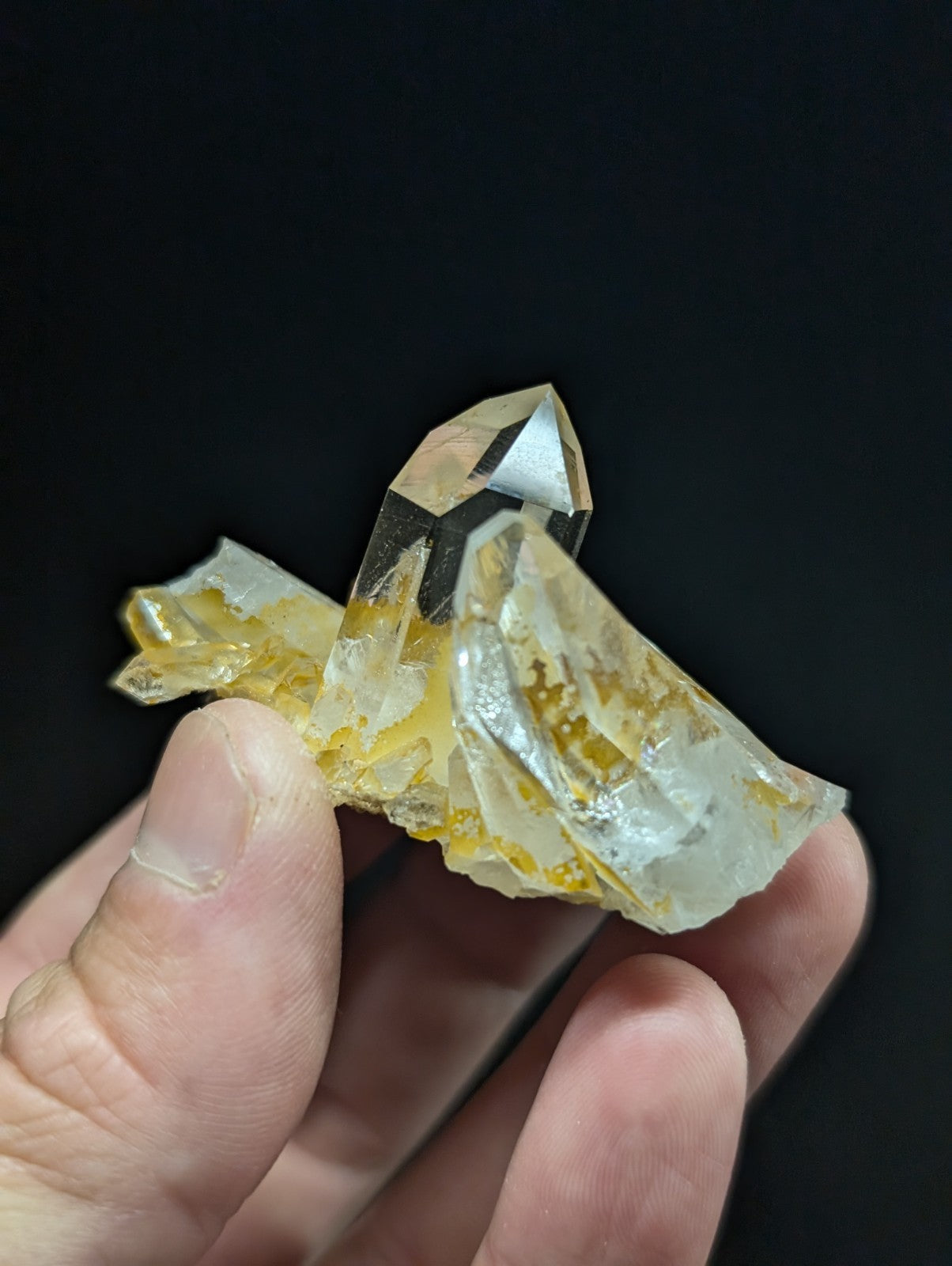 A translucent yellow and clear quartz crystal cluster with a pointed tip, held gently in someone’s hand.