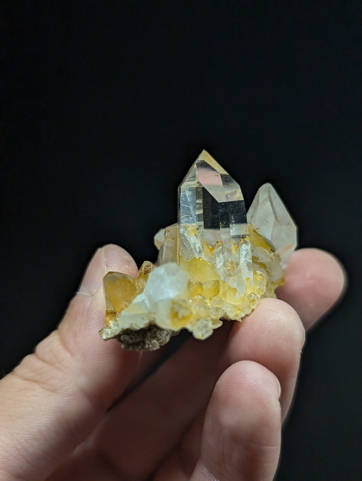 A translucent yellow and clear quartz crystal cluster with sharp, faceted points held in a hand.