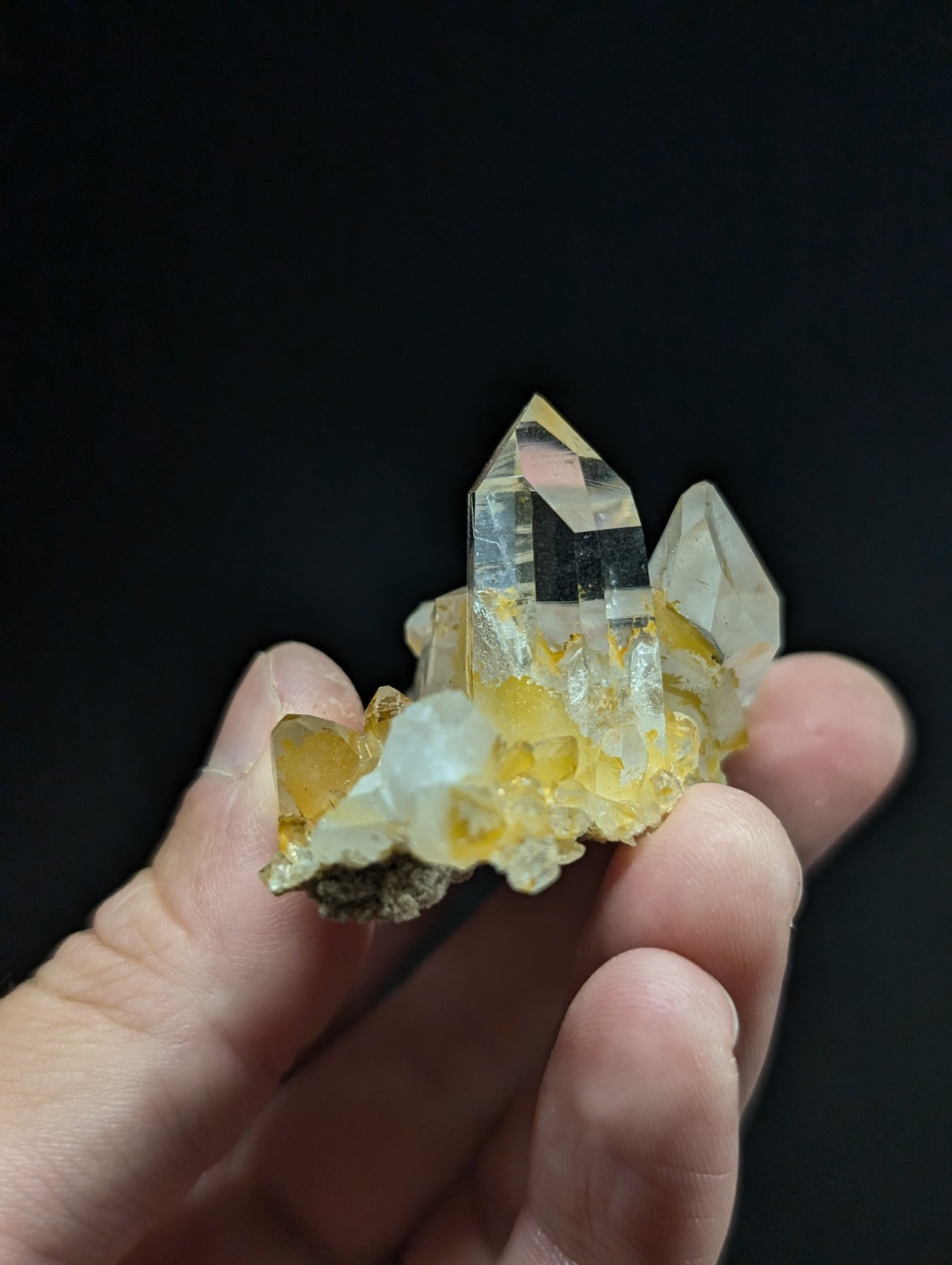 A translucent yellow and clear quartz crystal cluster with sharp, faceted points held in a hand.