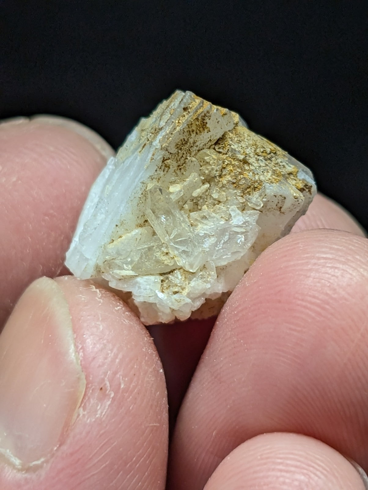 A translucent white mineral specimen with golden-yellow inclusions, held delicately between fingers.