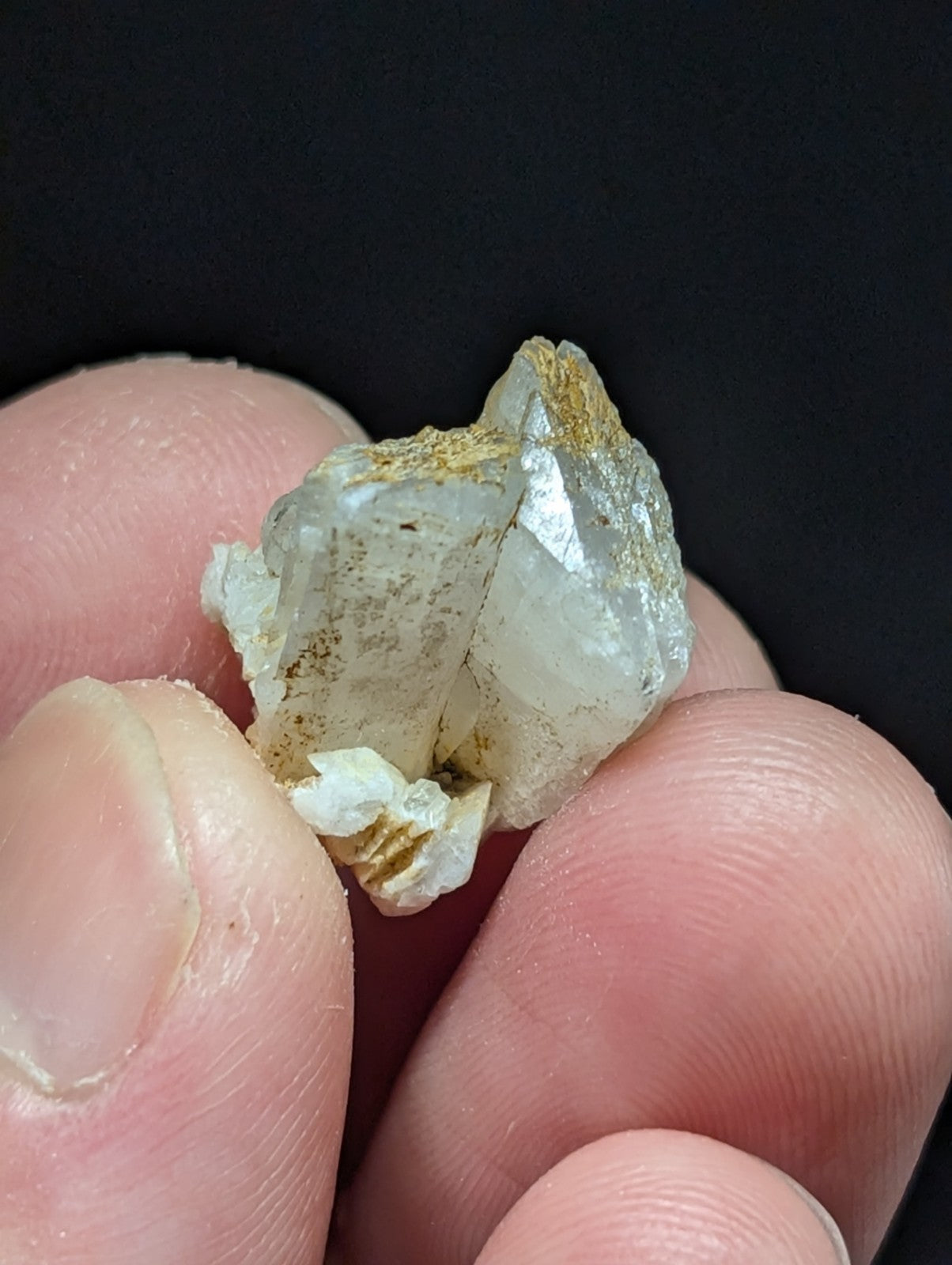 A translucent white quartz crystal with golden mineral inclusions, held gently between fingers.