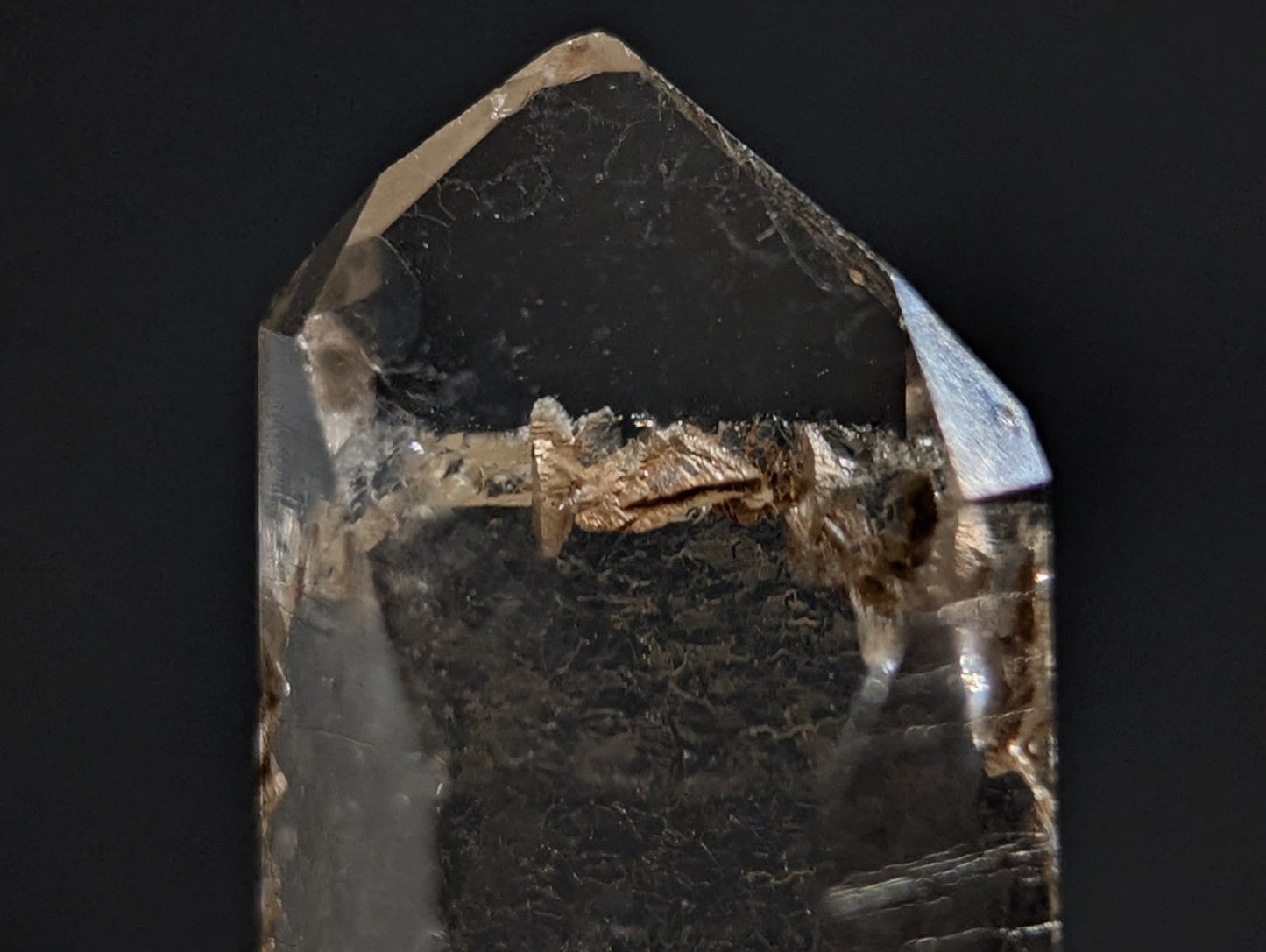 A translucent smoky quartz crystal with a pointed, faceted top and visible internal inclusions.