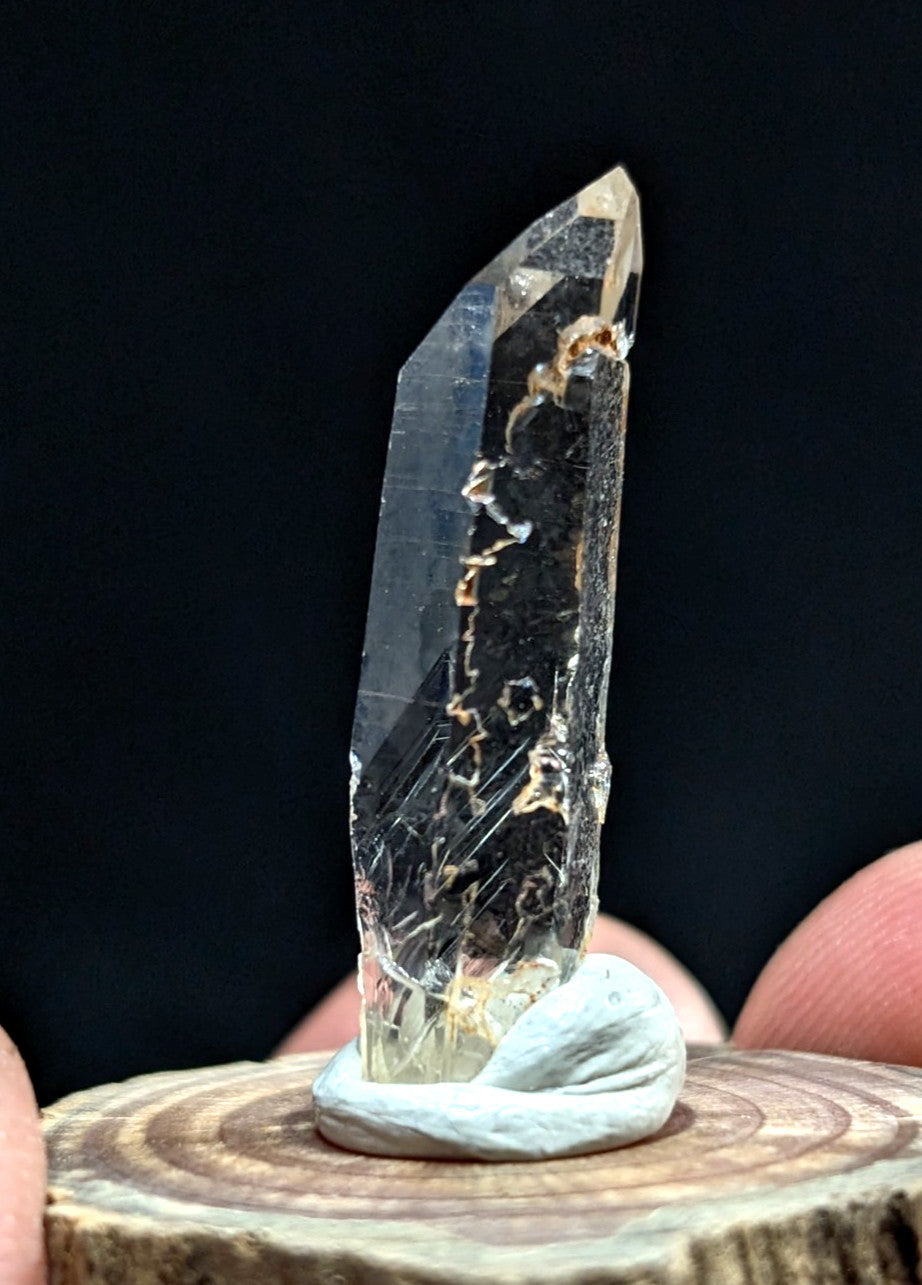 A clear quartz crystal with natural inclusions and a pointed tip, displayed on a wooden base.