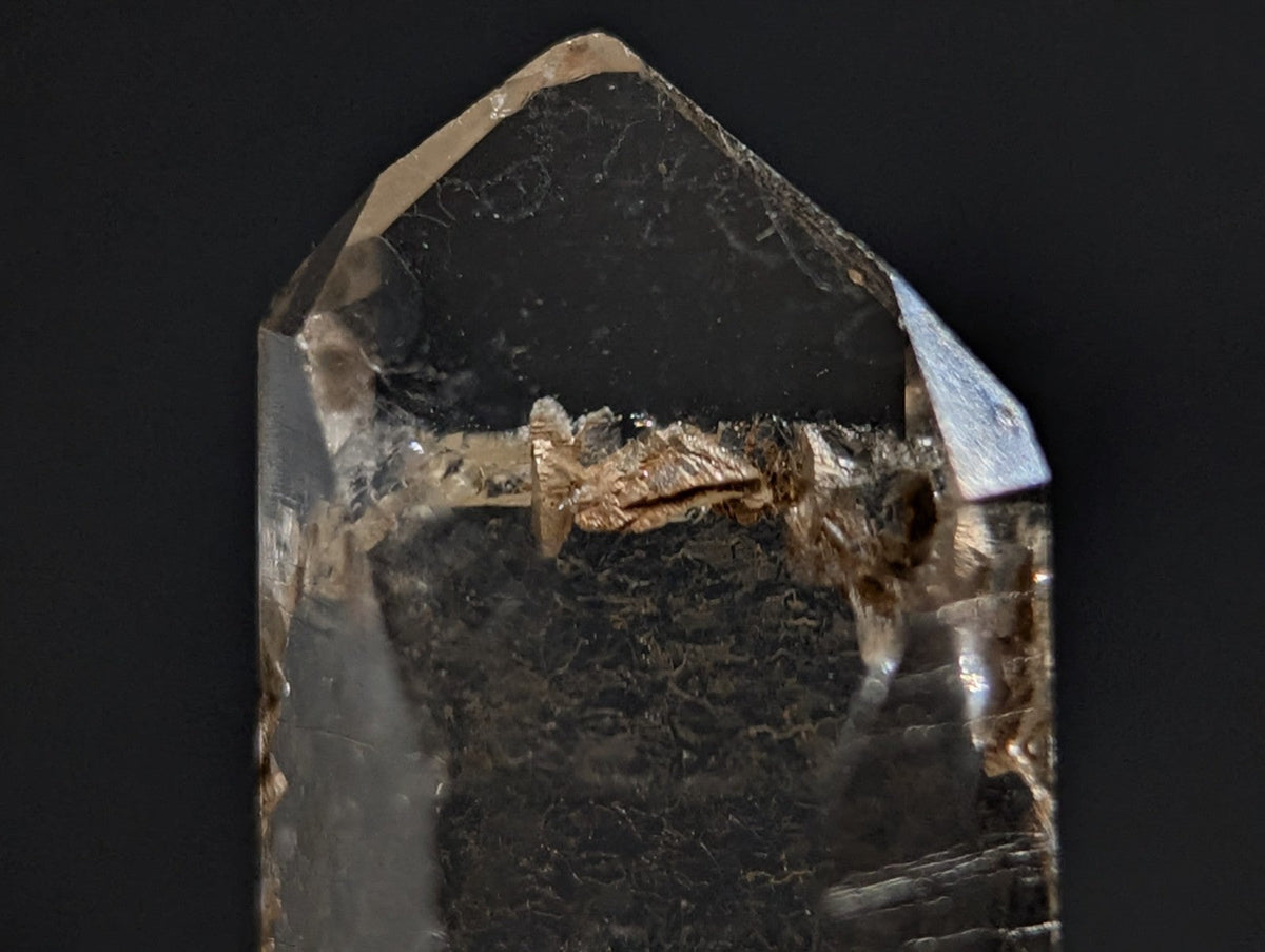 A translucent smoky quartz crystal with a pointed, faceted top and visible internal inclusions.