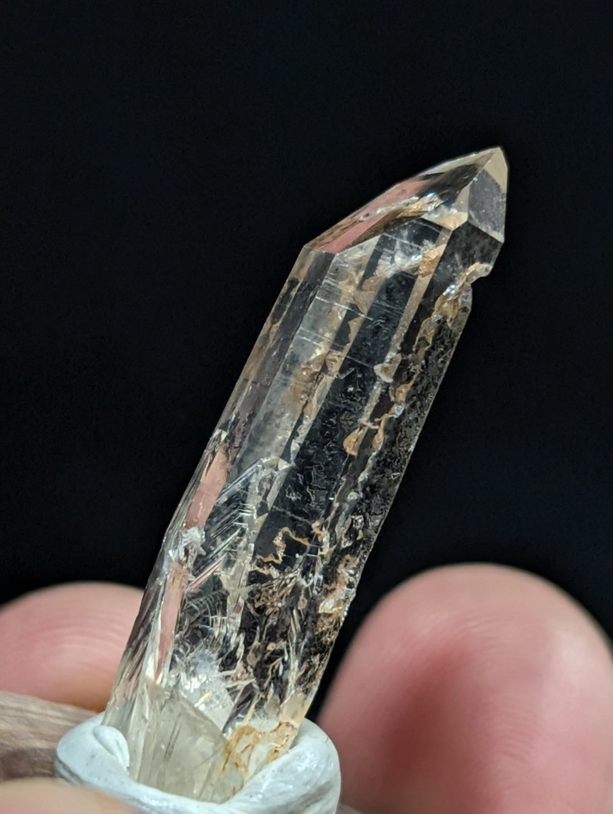 A clear quartz crystal with natural inclusions and a pointed tip, held securely by fingers.