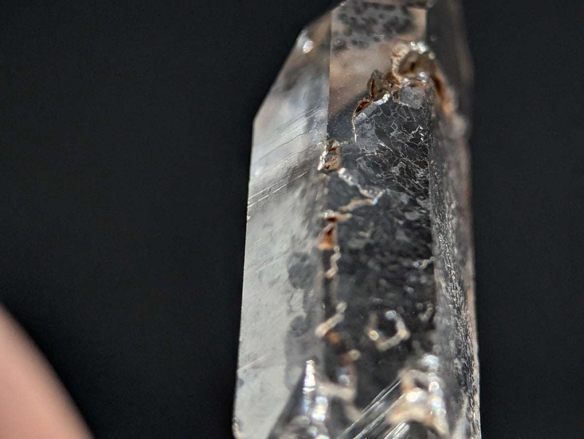 A translucent quartz crystal with natural inclusions and a pointed tip, featuring subtle brownish veining against its clear, glassy surface.