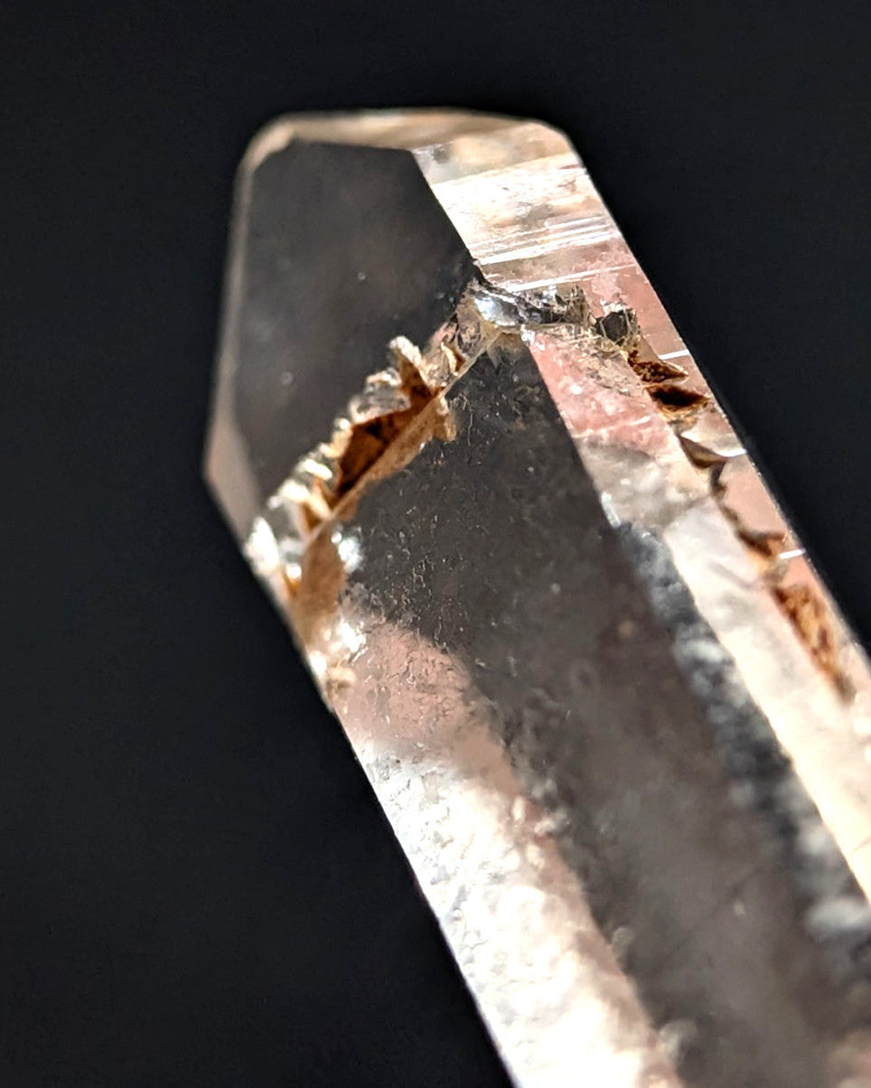 A translucent, clear quartz crystal with a natural, jagged fracture running through its center.