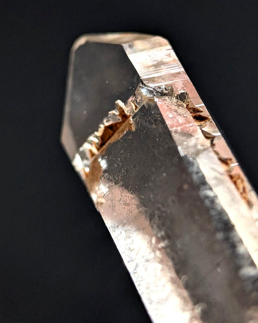 A translucent, clear quartz crystal with a natural, jagged fracture running through its center.