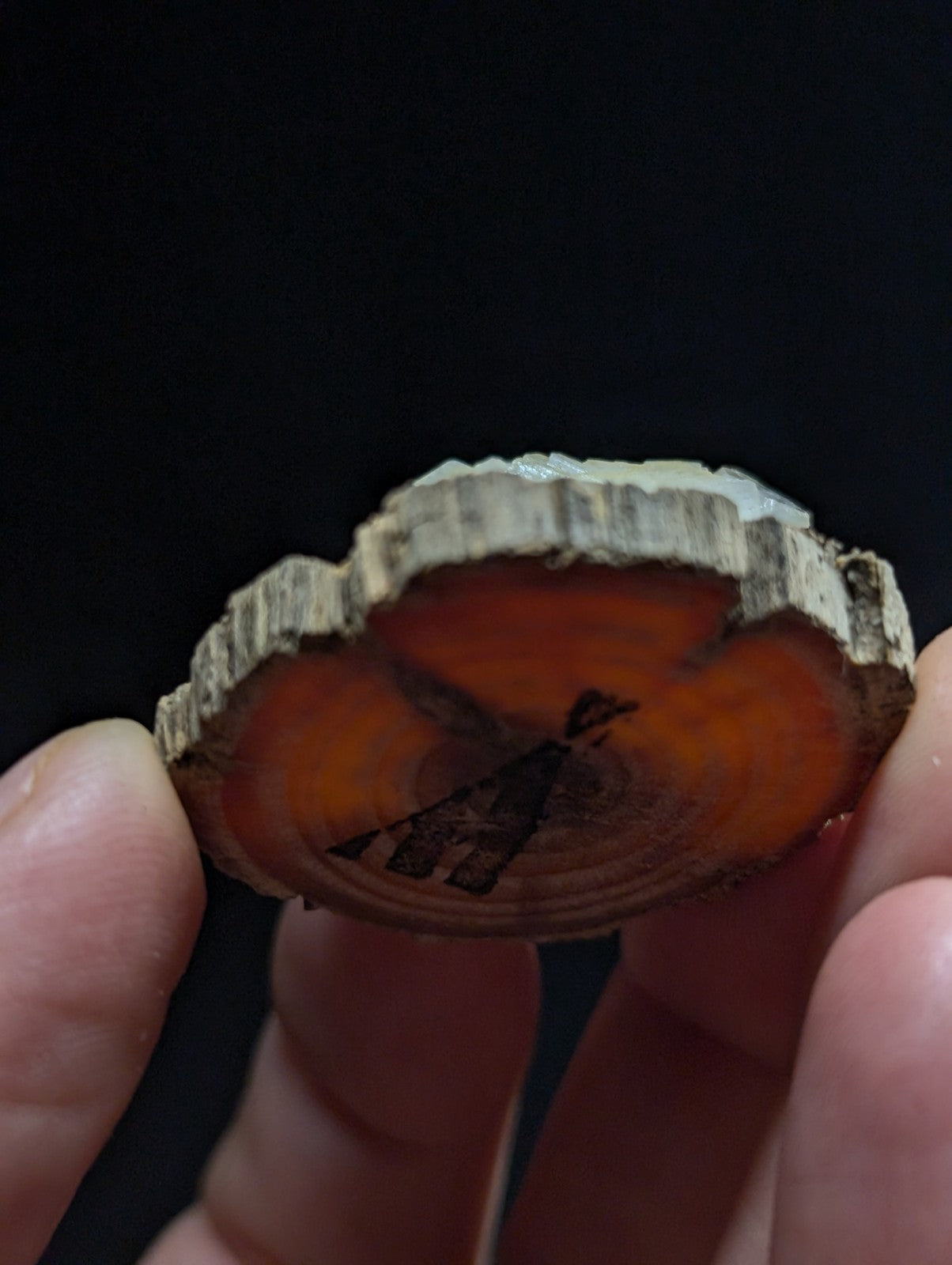 A circular wooden slice pendant with a natural bark edge, featuring an engraved silhouette of a figure against a warm orange-brown wood grain.