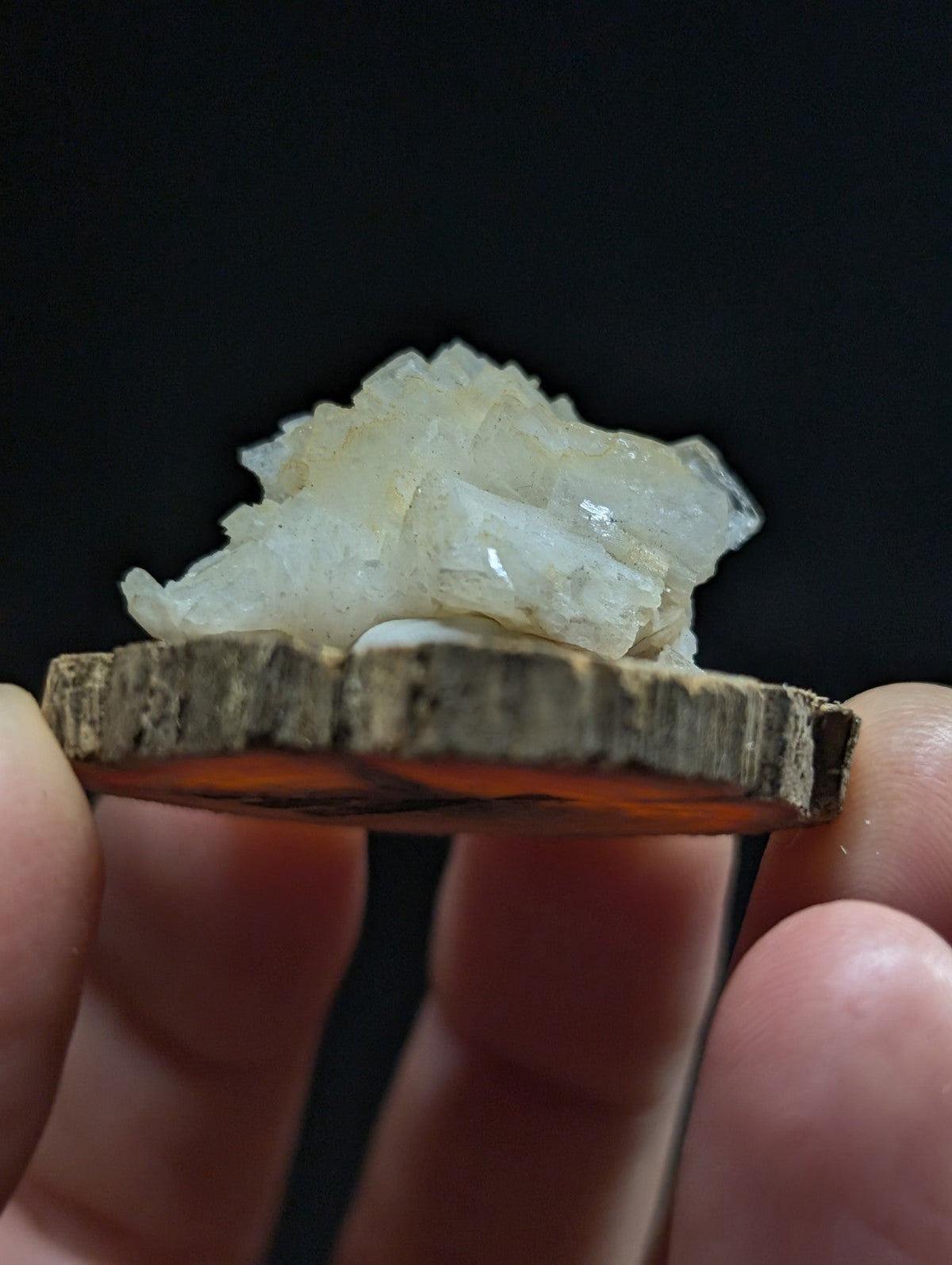 A translucent, crystalline mineral specimen with a pale, milky white hue rests atop a rustic wooden slice.