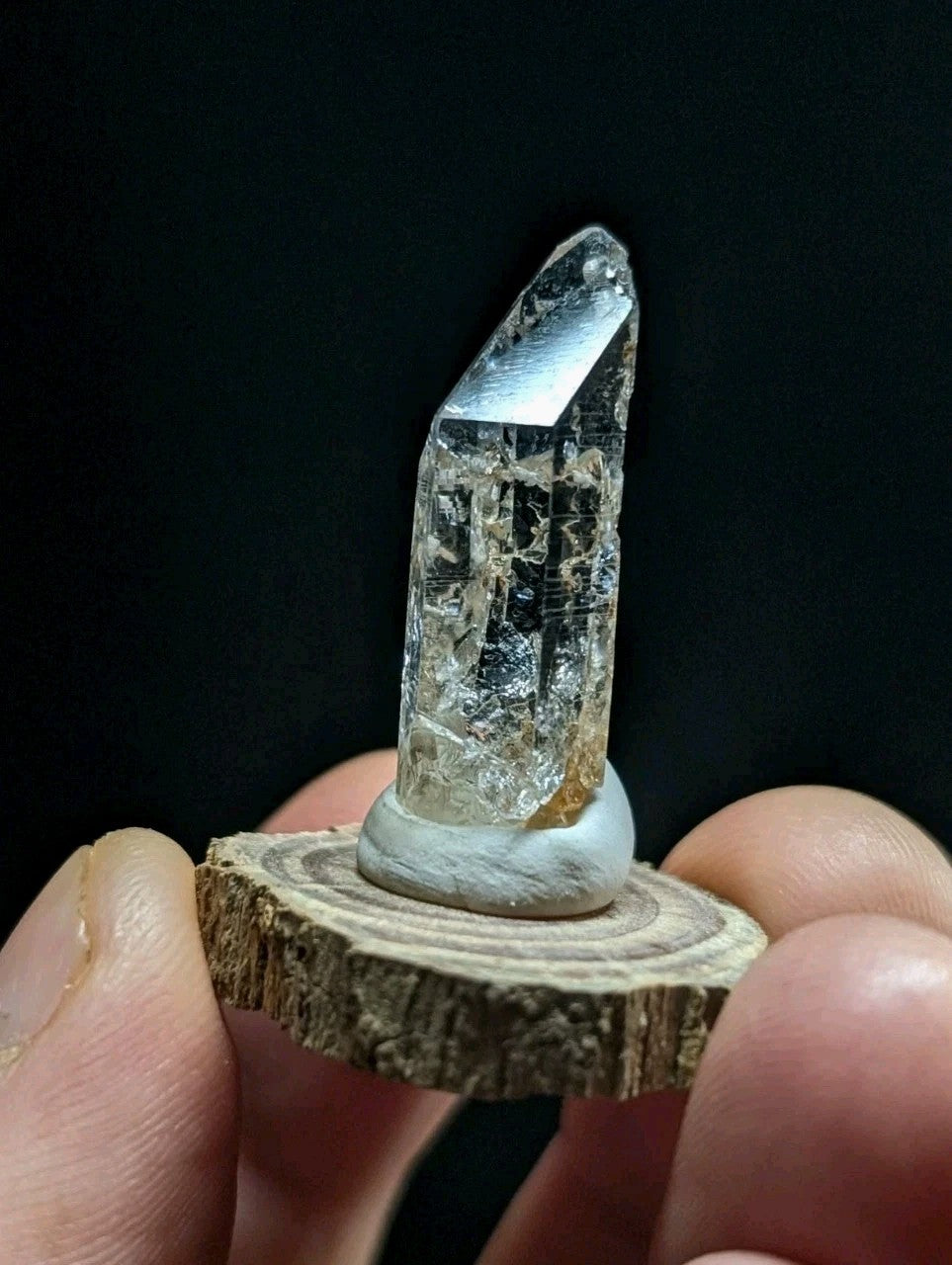 A clear quartz crystal with a faceted top and natural internal inclusions, mounted on a circular wooden base.