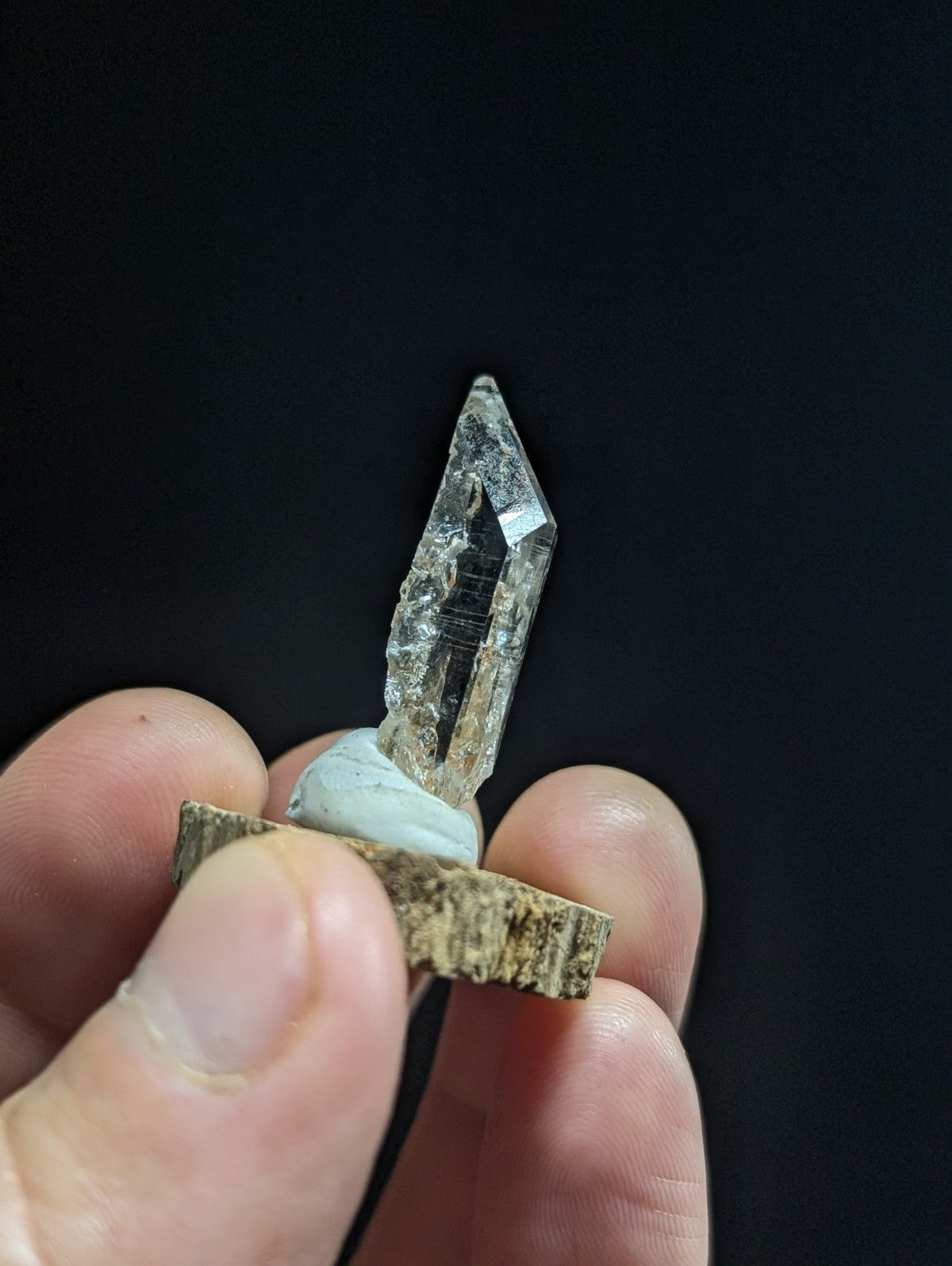 A clear, faceted quartz crystal with subtle internal striations is mounted on a rustic wooden base.