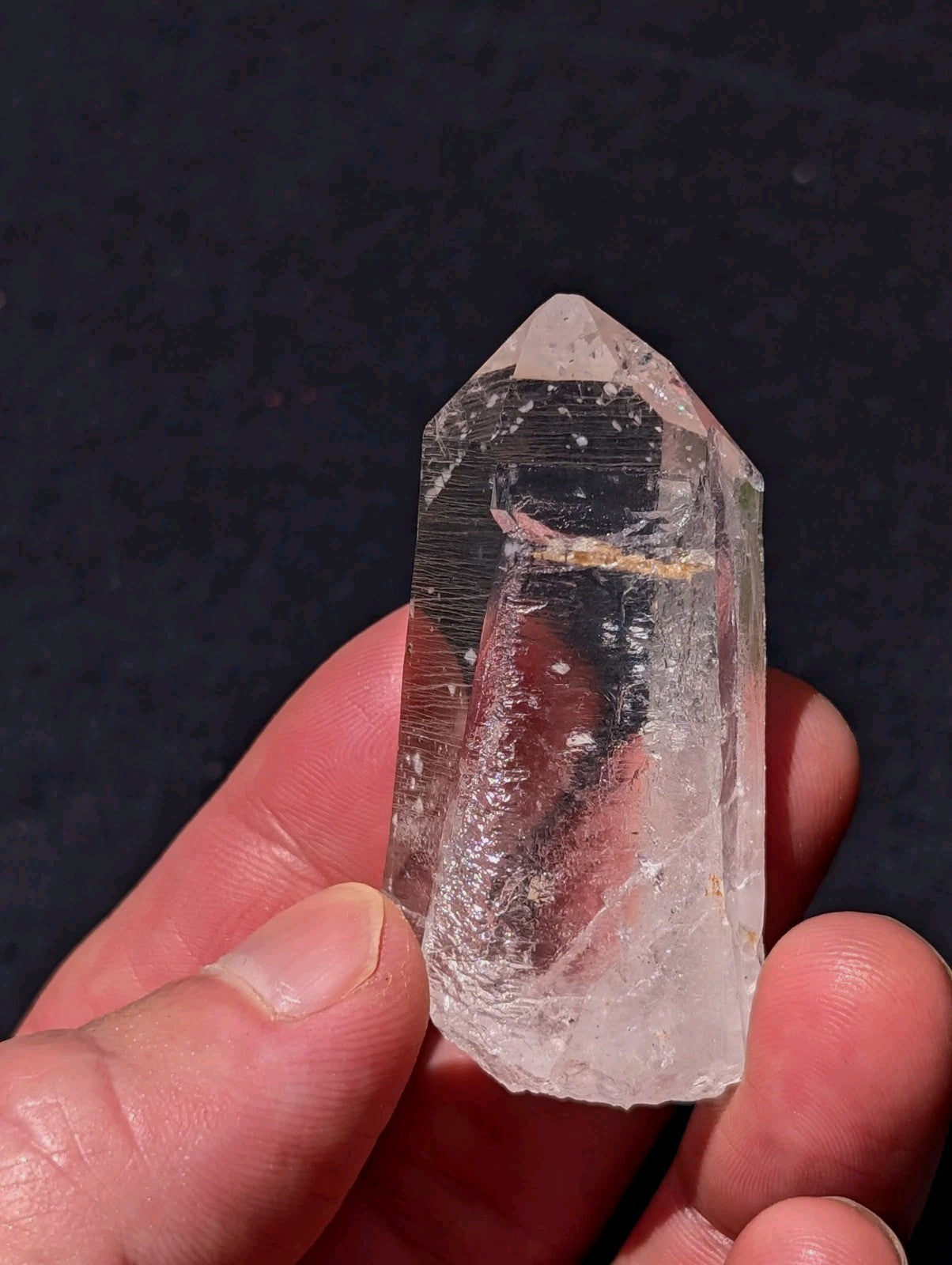 A clear quartz crystal with a pointed tip and natural inclusions, held gently between fingers.