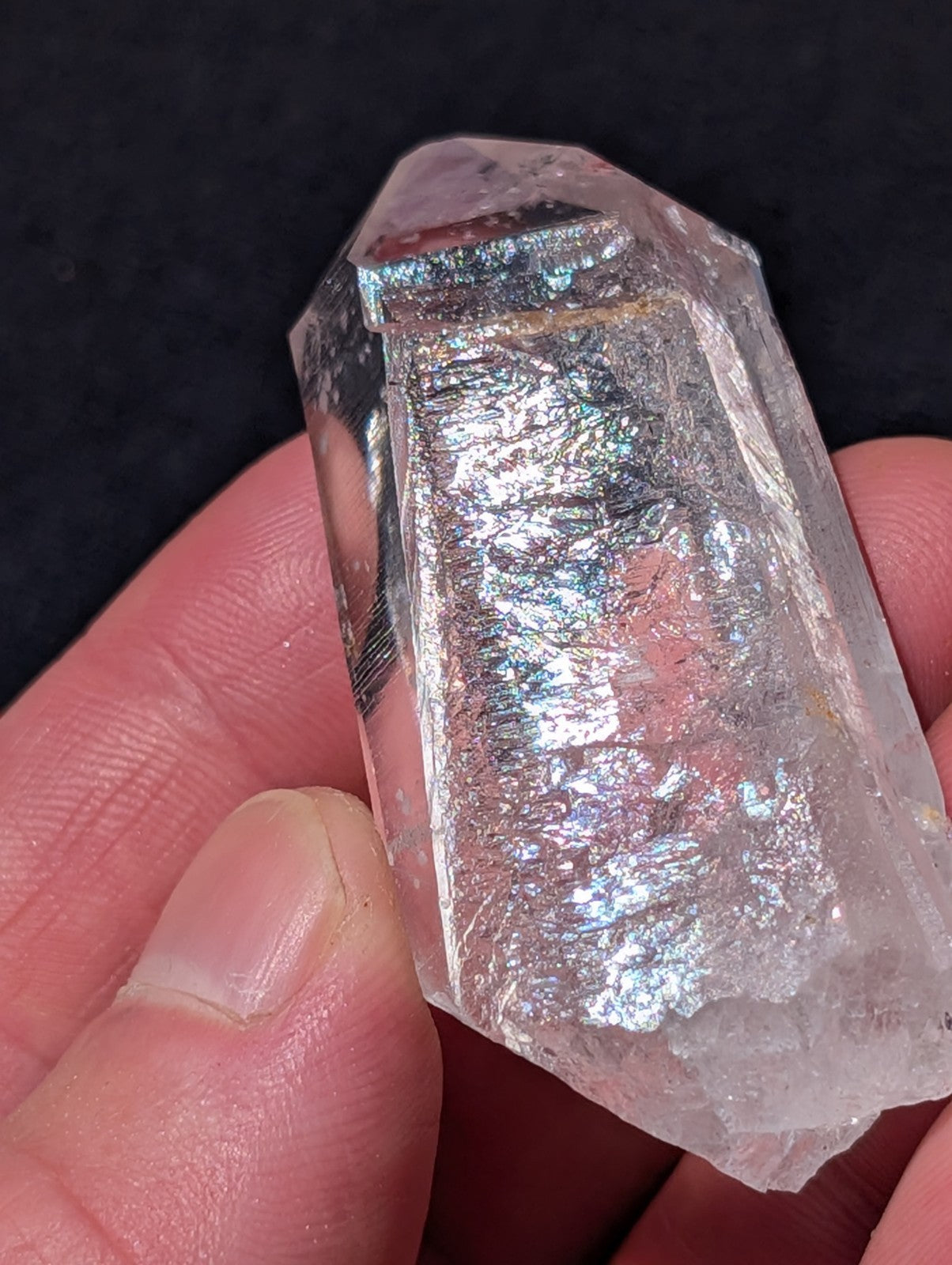 A translucent, clear quartz crystal with a faceted top and iridescent internal reflections.