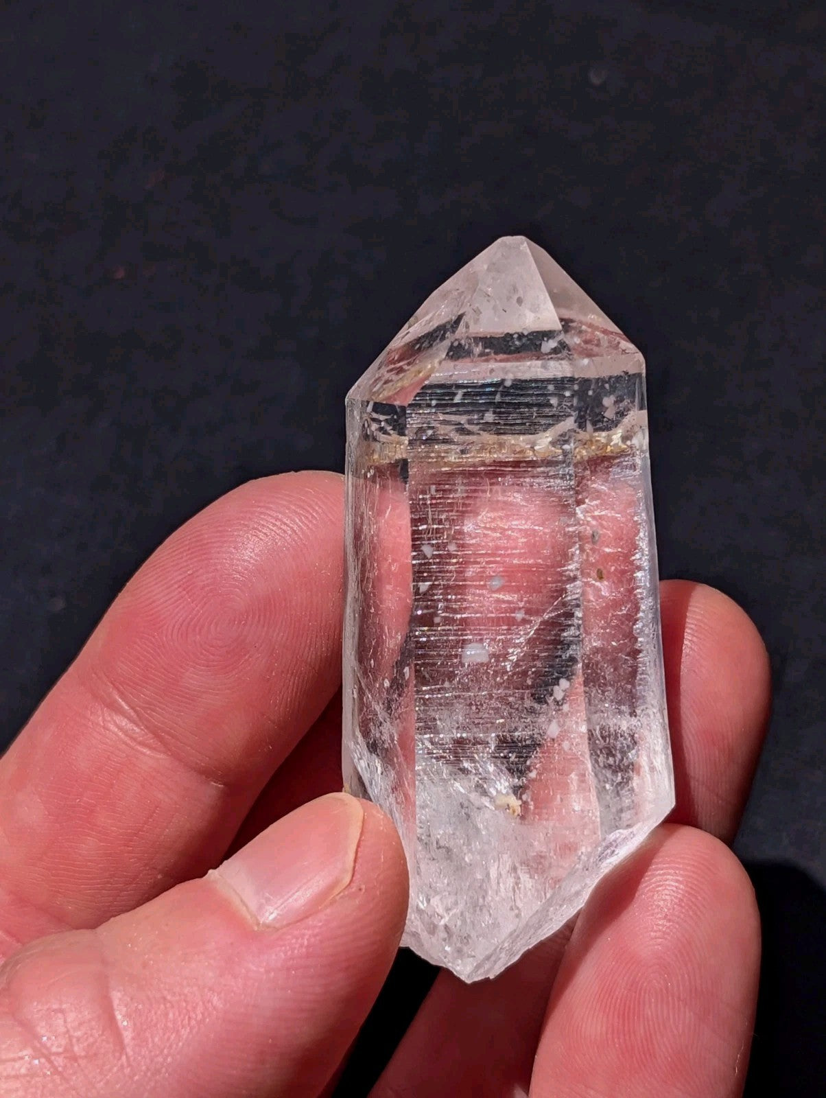 A clear, transparent quartz crystal with a pointed tip and natural internal striations.