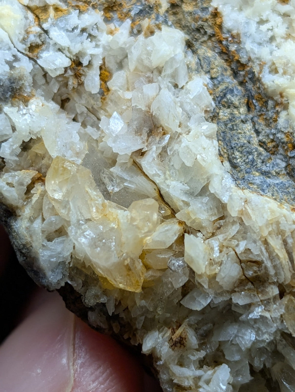 A cluster of translucent, crystalline quartz formations with a mix of clear and pale yellow hues growing from a darker, earthy rock matrix.