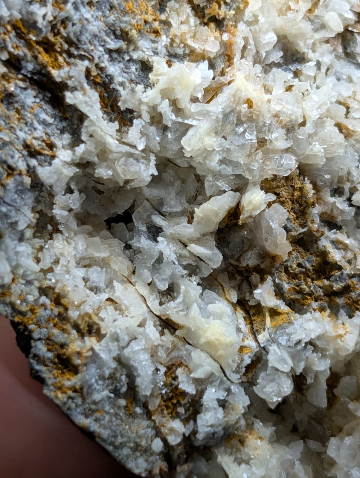 A cluster of translucent white crystals with jagged, interlocking formations set against a darker gray and yellowish matrix.