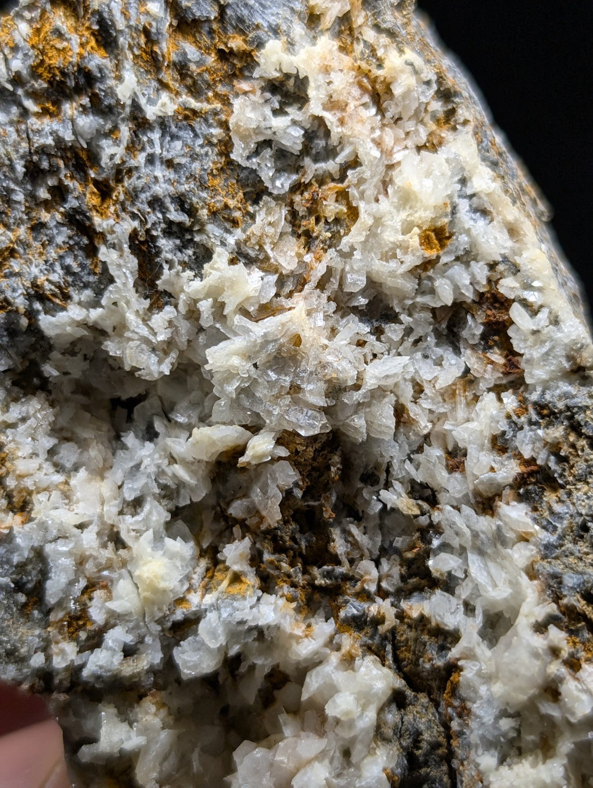 A rugged, naturally occurring mineral specimen featuring a dense cluster of translucent white crystals interwoven with patches of earthy gray and rusty orange hues.