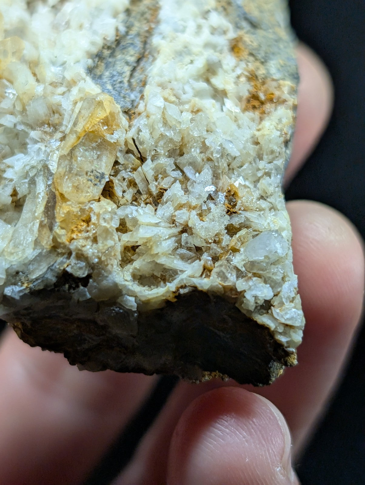 A hand holds a rough, irregularly shaped mineral specimen featuring translucent white and pale yellow crystalline formations embedded in a darker matrix.