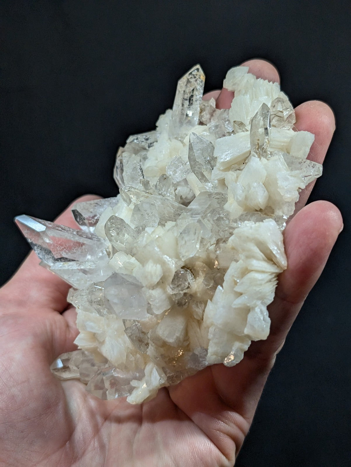 A hand holds a cluster of clear quartz crystals with some exhibiting milky white inclusions and sharp, pointed facets.