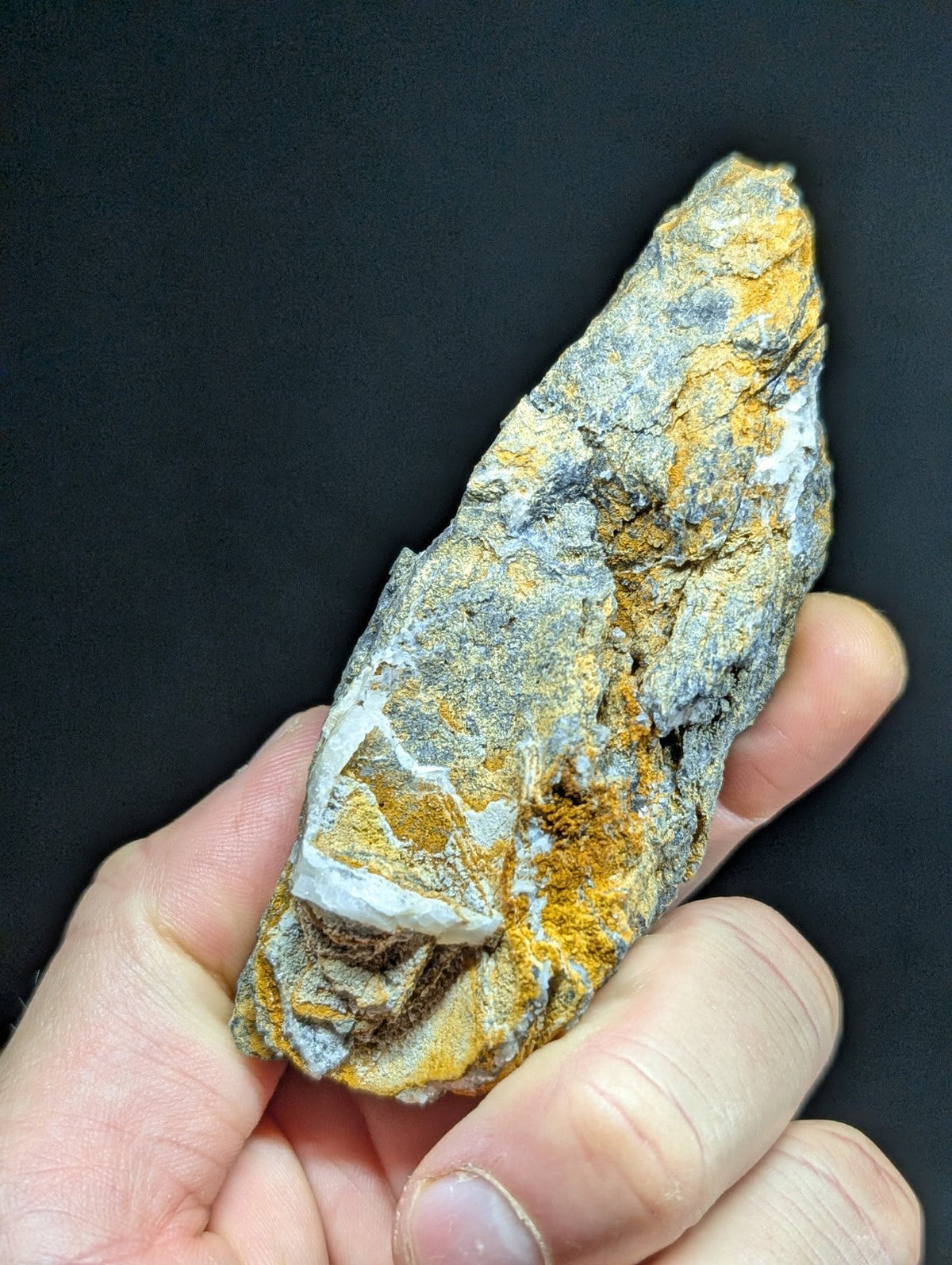 A rugged, irregularly shaped rock with a mottled surface of gray, white, and vibrant orange-yellow patches.