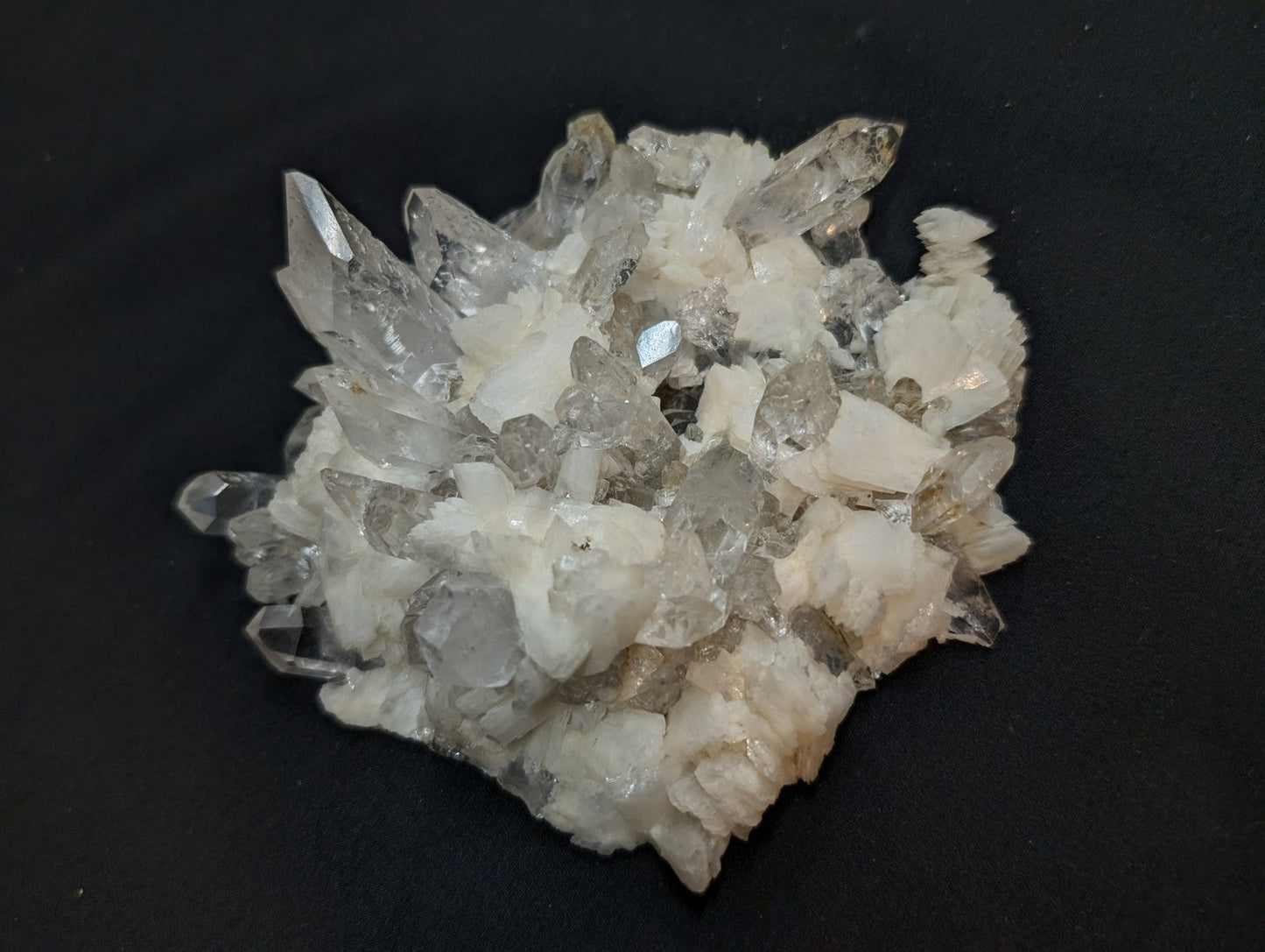 A cluster of clear, translucent quartz crystals with sharp, pointed tips and a mix of white and pale gray hues.