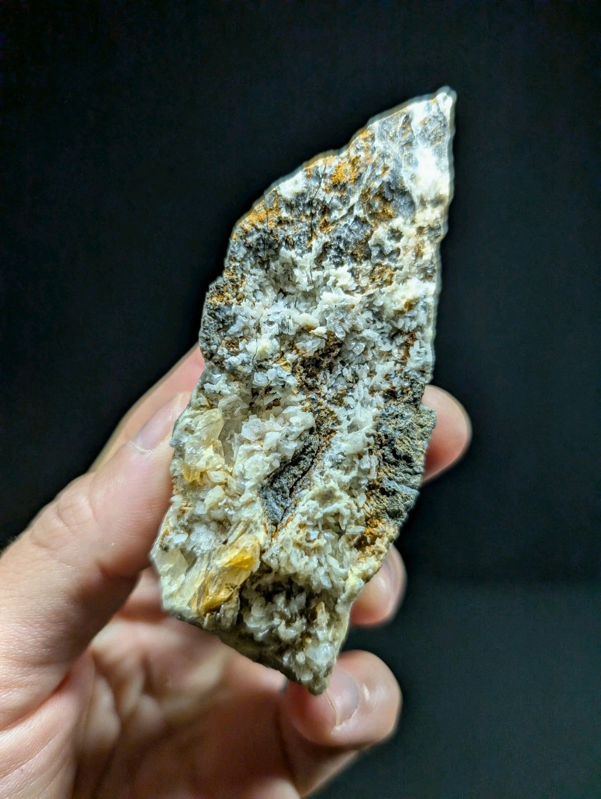 A rugged, irregularly shaped mineral specimen with a mottled surface of white, gray, and patches of yellowish-orange.