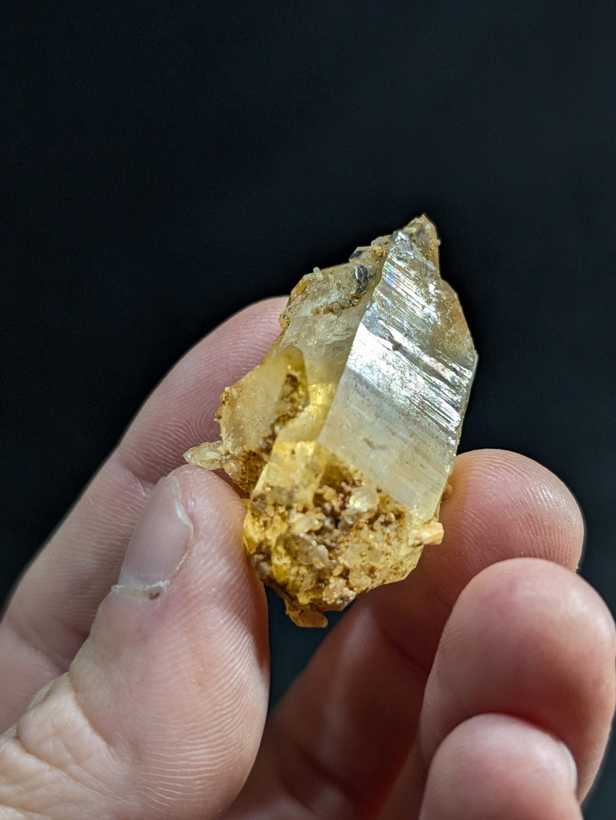 A translucent golden-yellow quartz crystal with a sharp, faceted point and rough, earthy matrix.