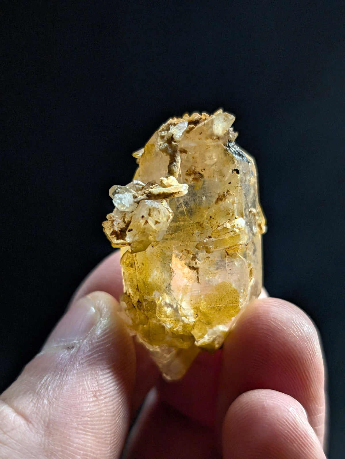 A translucent yellow crystal with natural imperfections and embedded mineral inclusions, held gently between fingers.