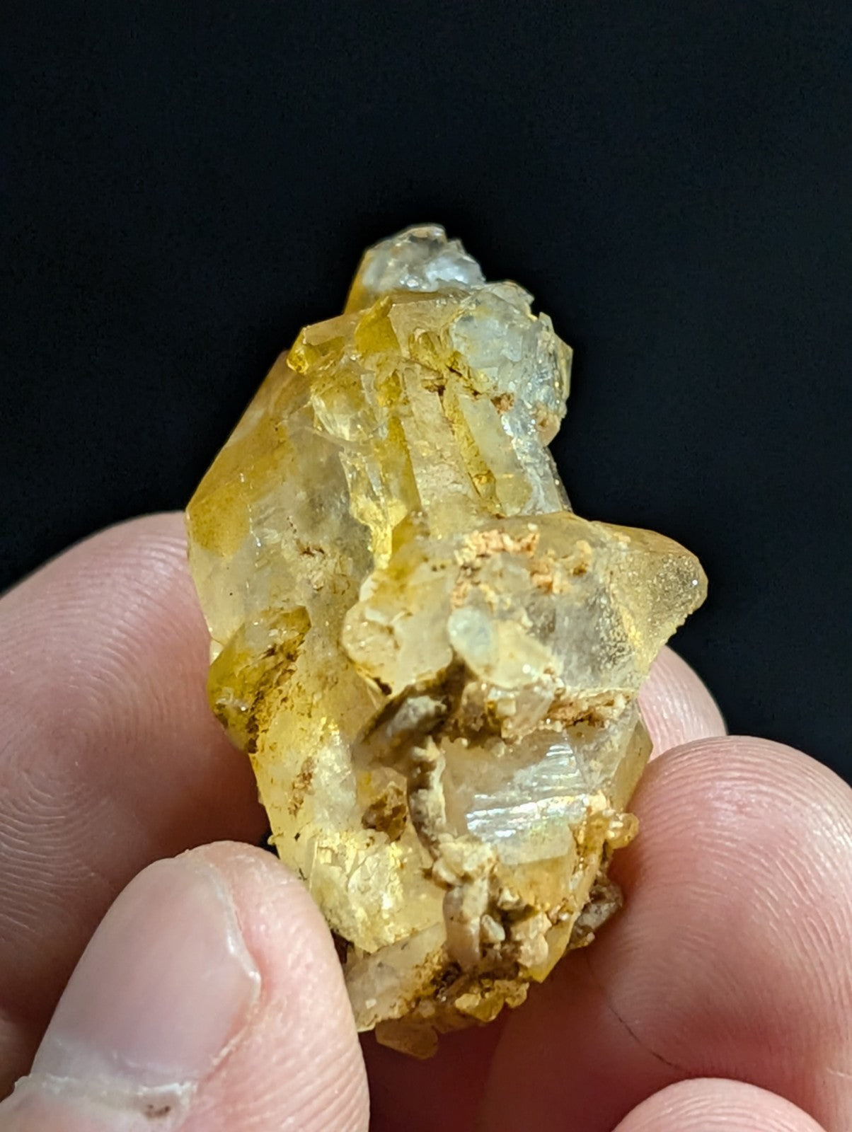 A translucent yellowish crystal cluster with embedded golden mineral inclusions, held gently between fingers.