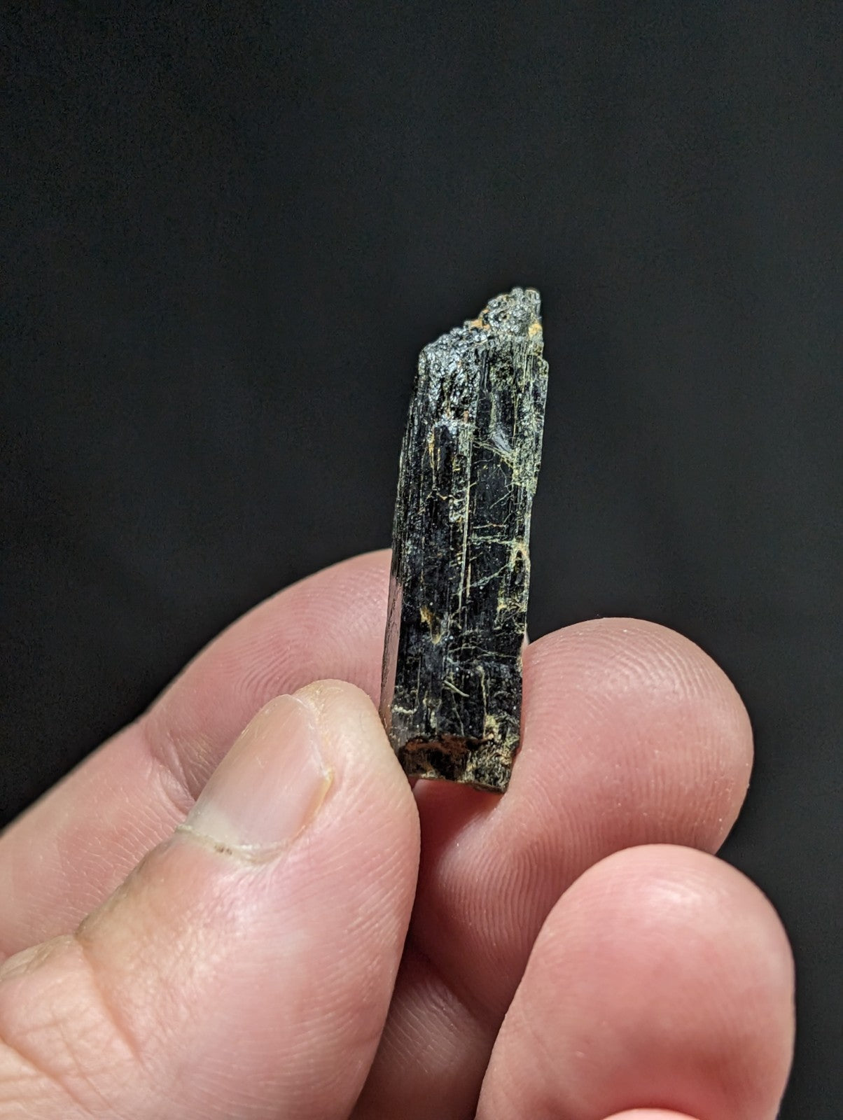 A dark green, translucent mineral crystal with visible striations and a rough, jagged top edge.