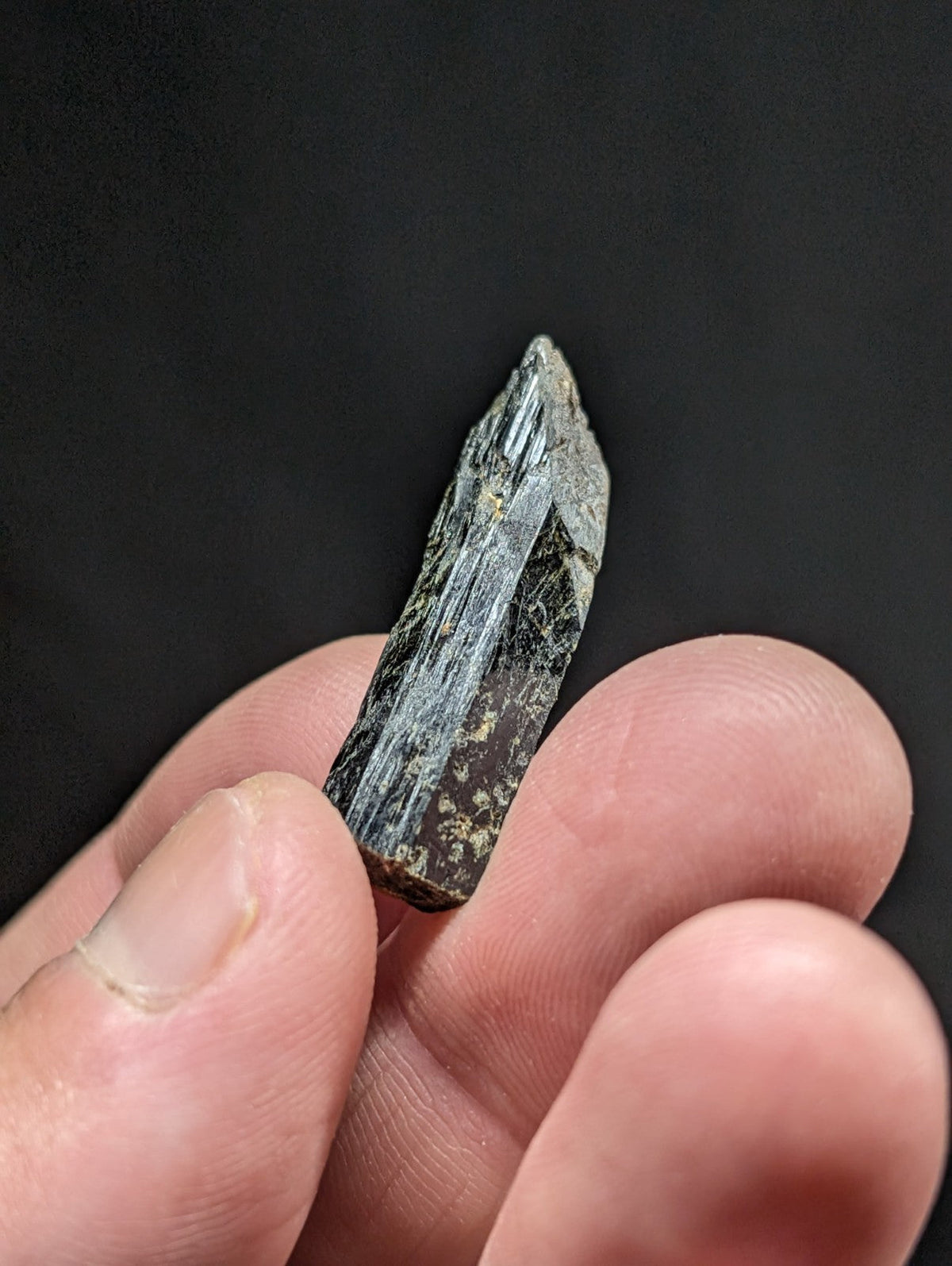 A dark green, translucent mineral crystal with visible striations and a pointed tip.