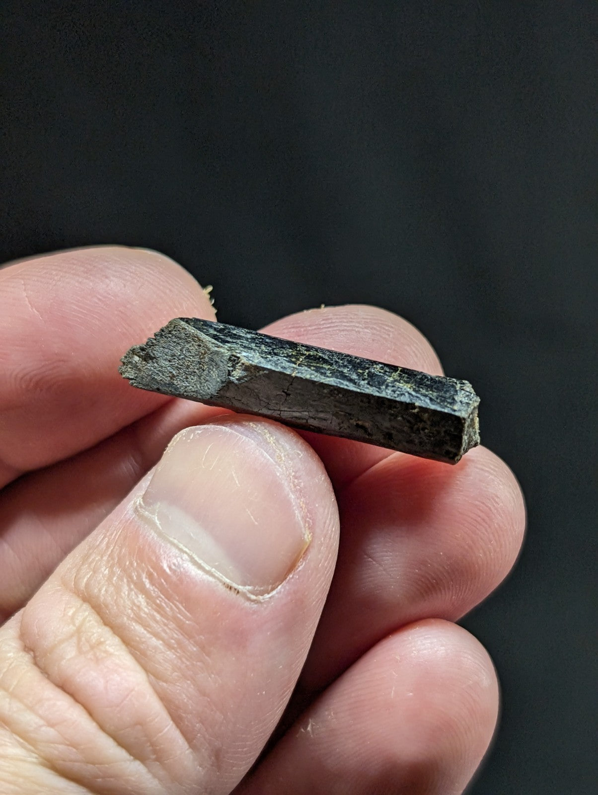 A dark, rough-textured mineral crystal with a rectangular prism shape and visible natural facets.