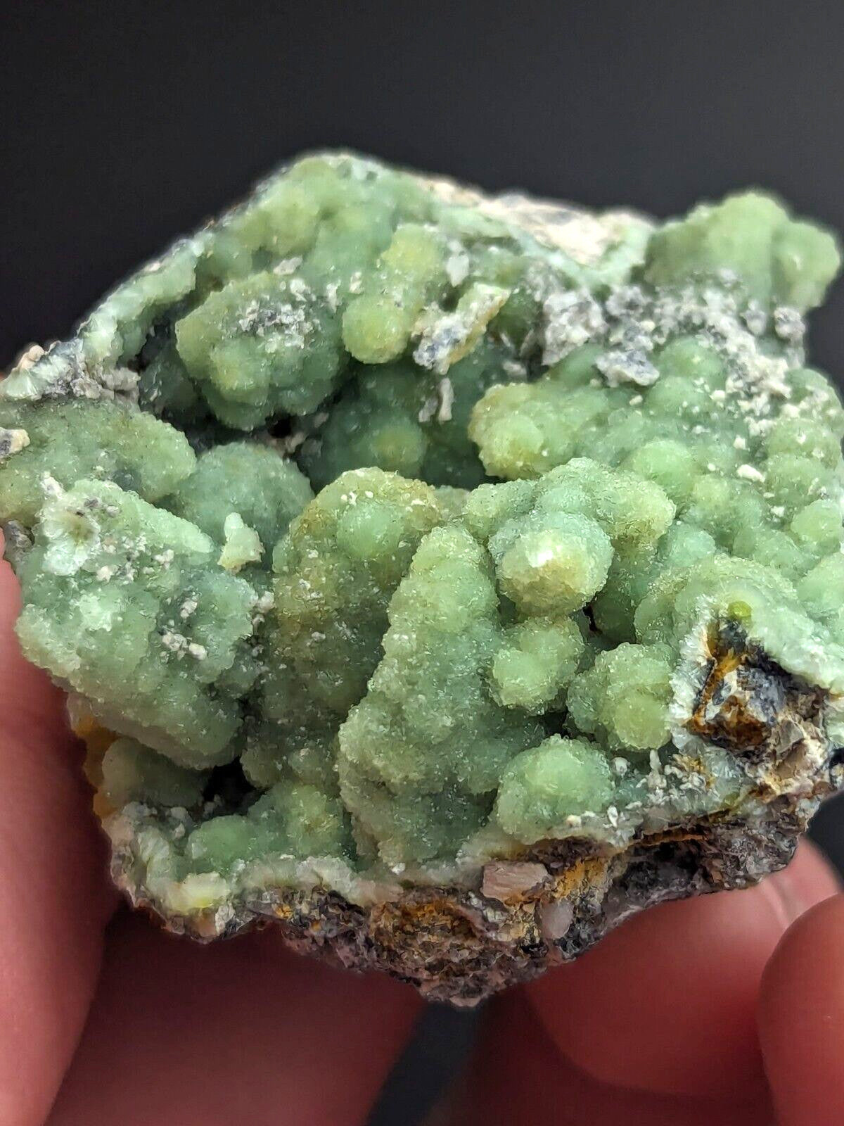 A hand holds a vibrant green mineral specimen featuring clustered, crystalline formations with some translucent and opaque areas.