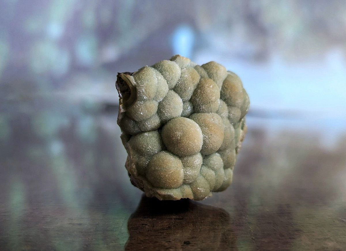A textured, pale greenish-gray mineral specimen with a clustered, bubble-like surface.