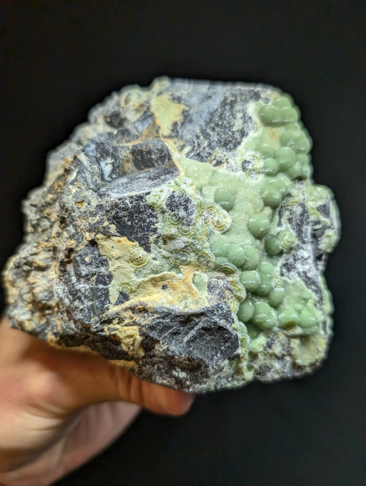 A rough, irregularly shaped mineral specimen featuring a striking contrast of dark gray rock with patches of vibrant green and yellowish hues.