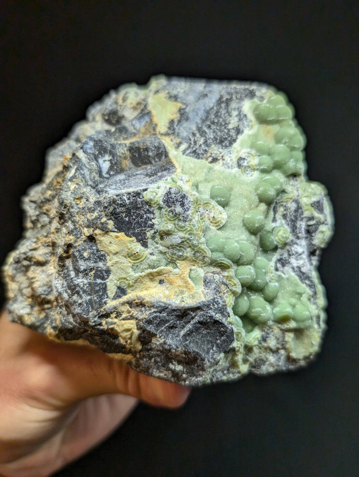A rough, irregularly shaped mineral specimen featuring a striking contrast of dark gray rock with patches of vibrant green and yellowish hues.
