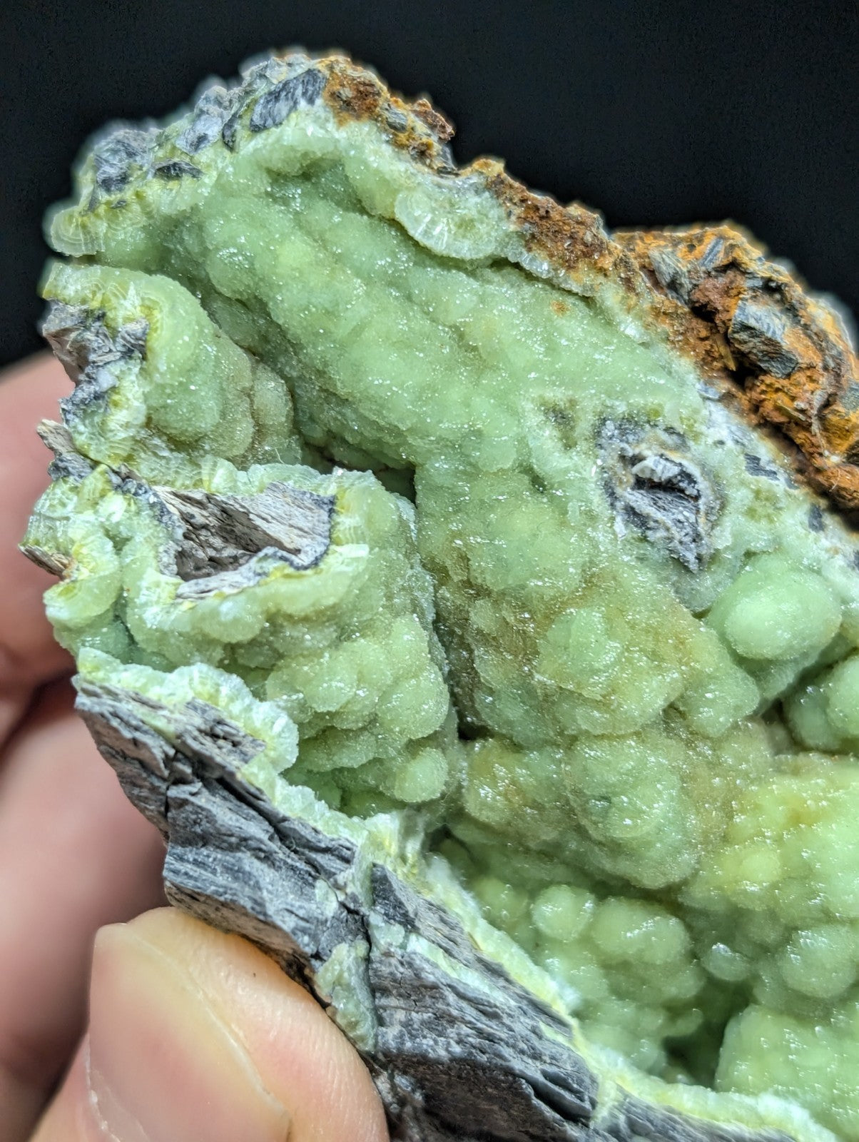 A pale green, crystalline mineral specimen with a rough, textured surface and earthy brownish-orange matrix.