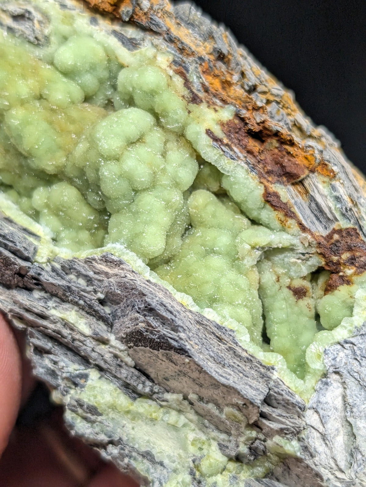A vibrant green, crystalline mineral formation with a rough, textured surface and earthy brownish-orange matrix.