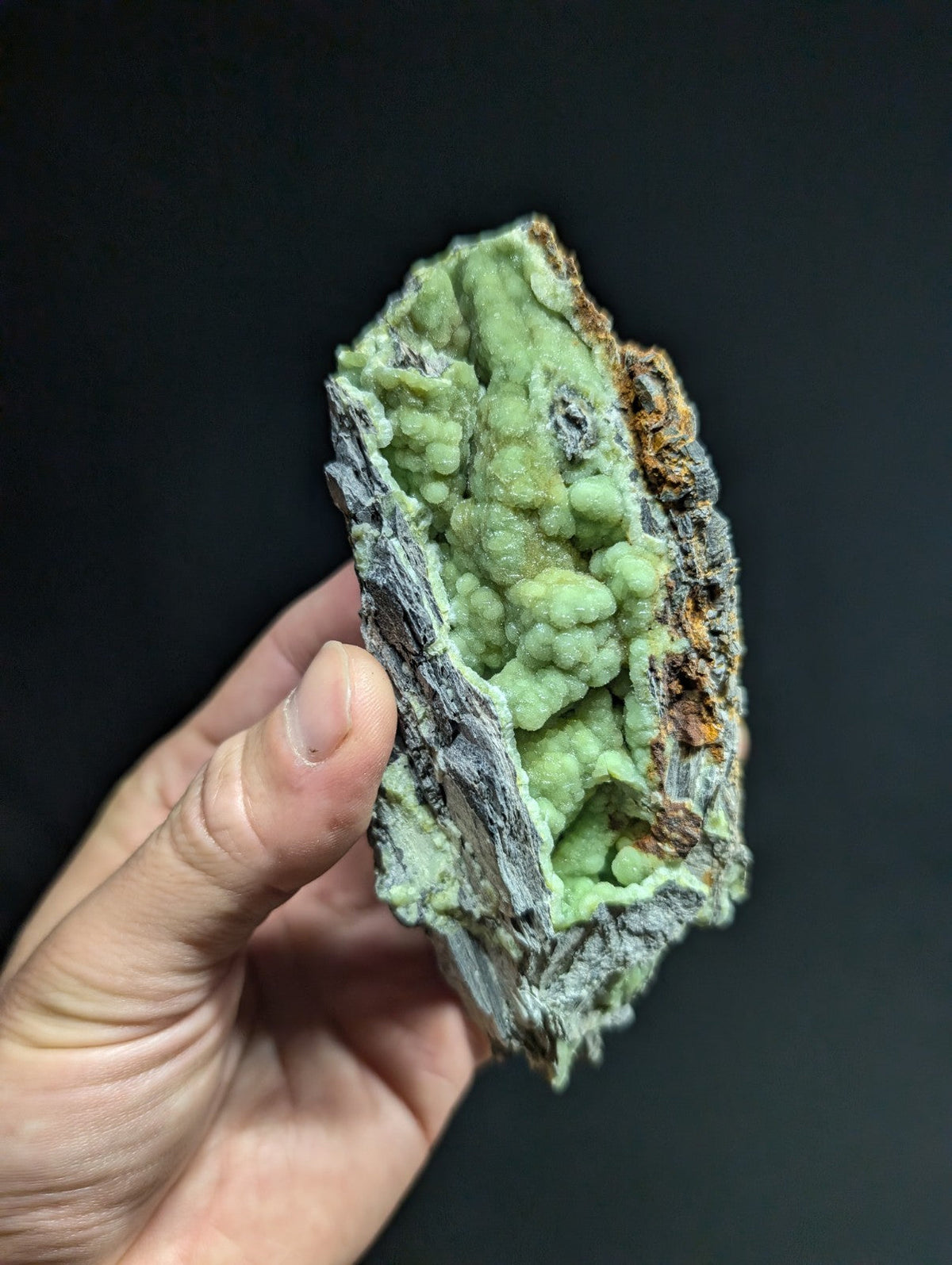 A hand holds a striking green mineral specimen with textured, bumpy formations against a dark background.
